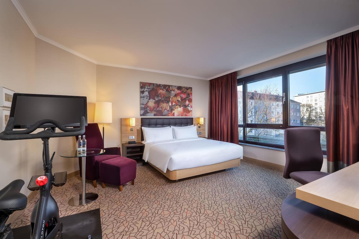 Una habitación de hotel con una cama, un escritorio, una silla, un televisor y una caminadora.