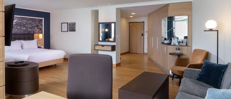 A hotel room with a bed, bedside table, lamp, and a seating area with a sofa and armchair.