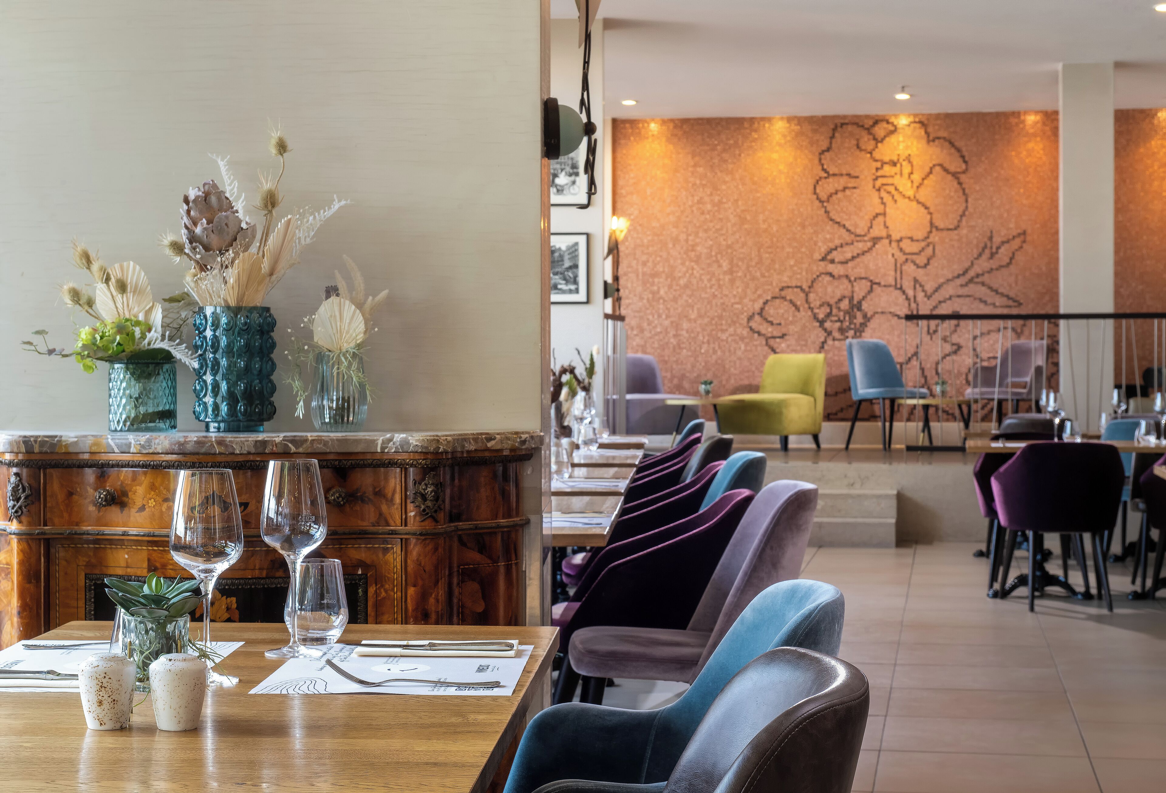 A restaurant with a wooden table set for dining, a wall with a floral mural, and a seating area with chairs.