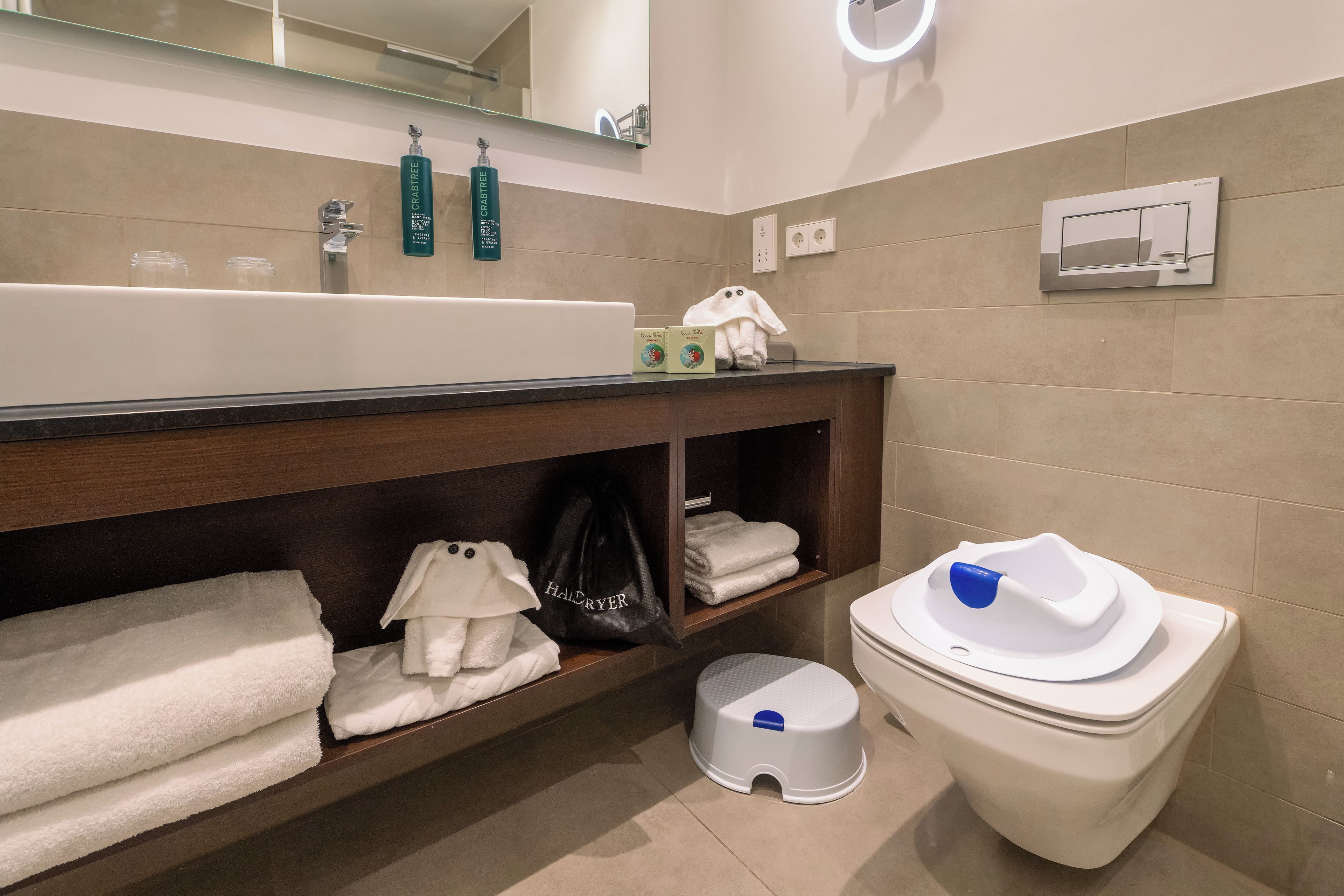 Un baño moderno con un lavamanos grande, un inodoro y un estante con toallas y un secador de pelo.