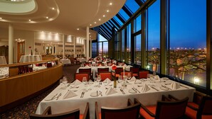 A restaurant with tables set for dining, large windows, and a view of the cityscape. - Hilton Mainz (Mainz)