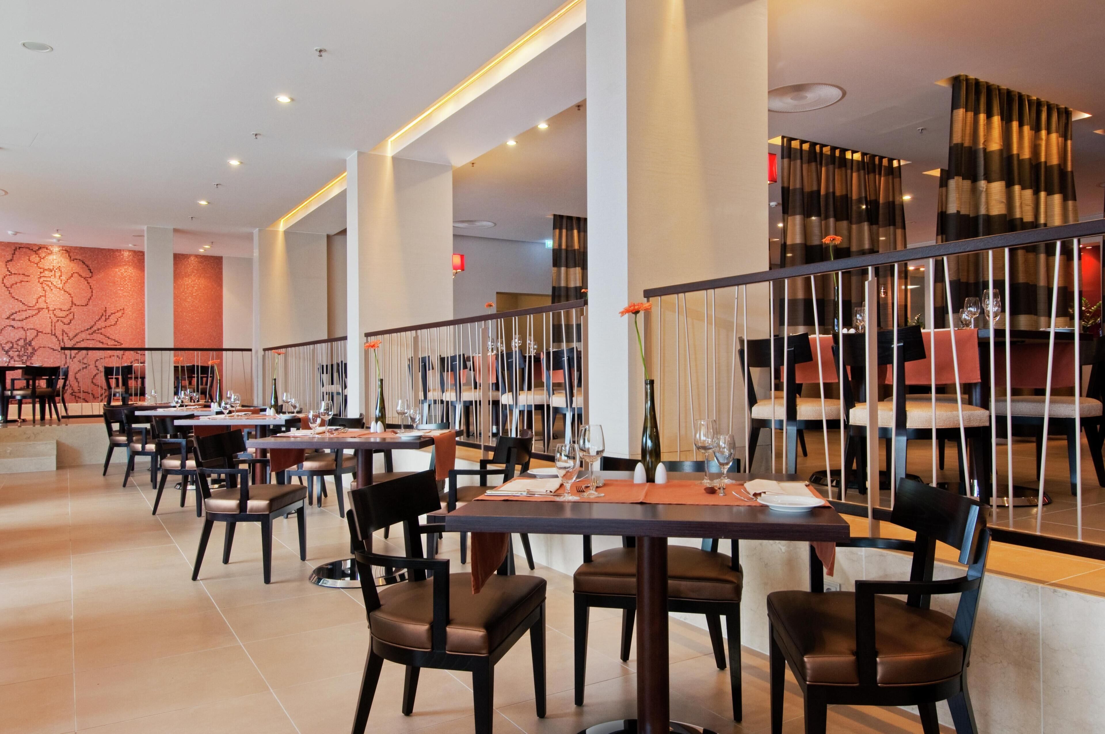 A restaurant with multiple tables and chairs, a staircase, and a decorative wall.