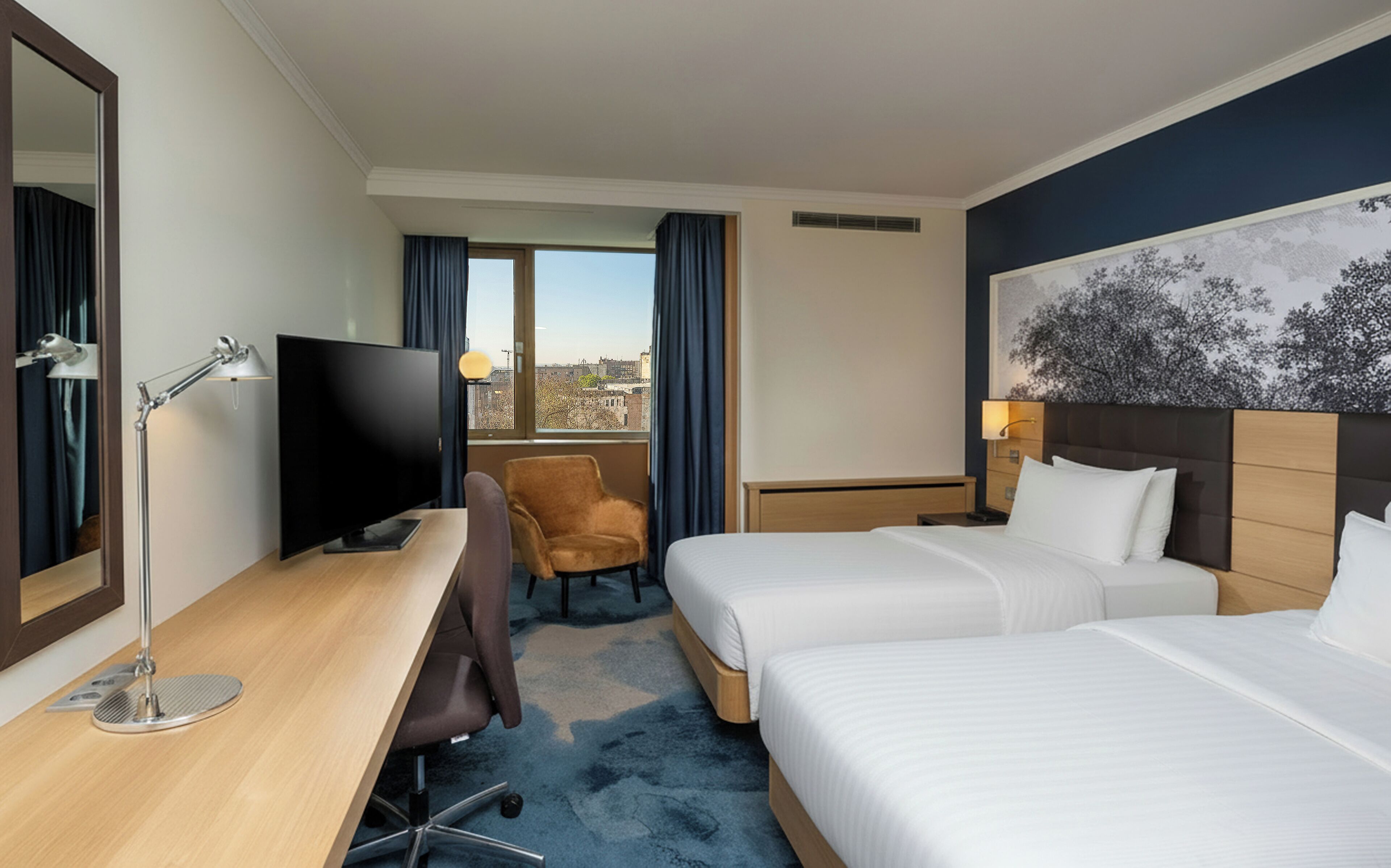A hotel room with a desk, two beds, a TV, a chair, and a window with curtains.