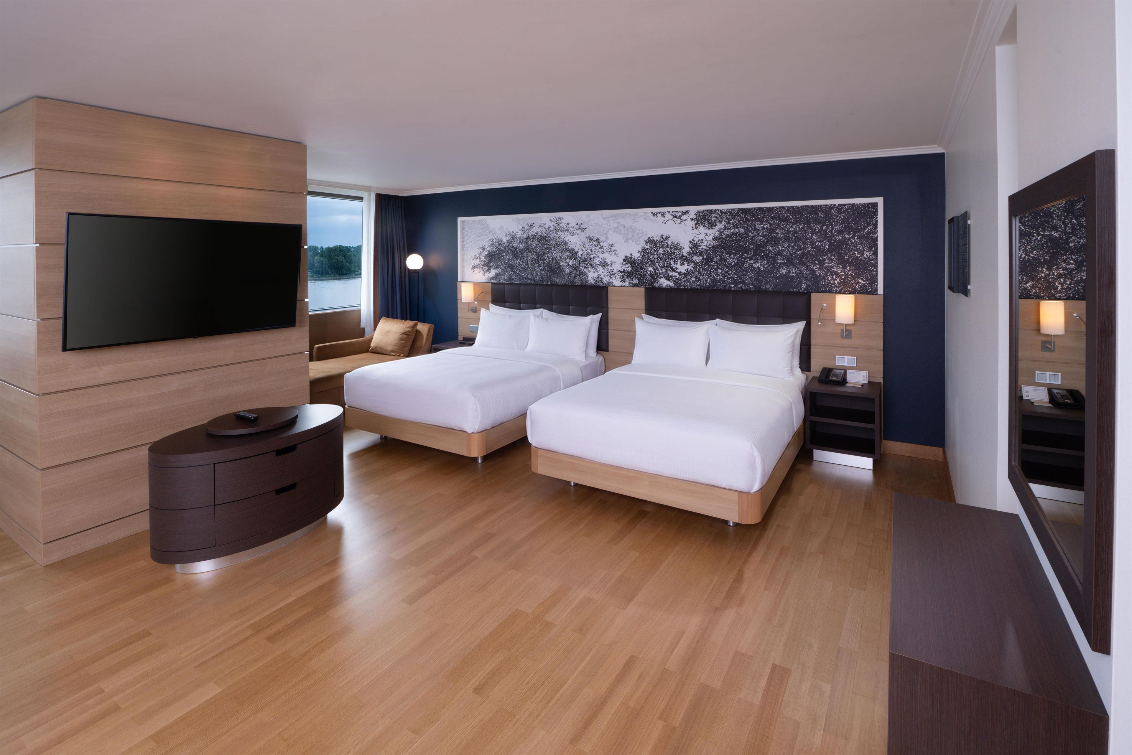 Ein Hotelzimmer mit zwei Betten, einem Flachbildfernseher, einem Holzschrank und einem großen Fenster mit Blick.