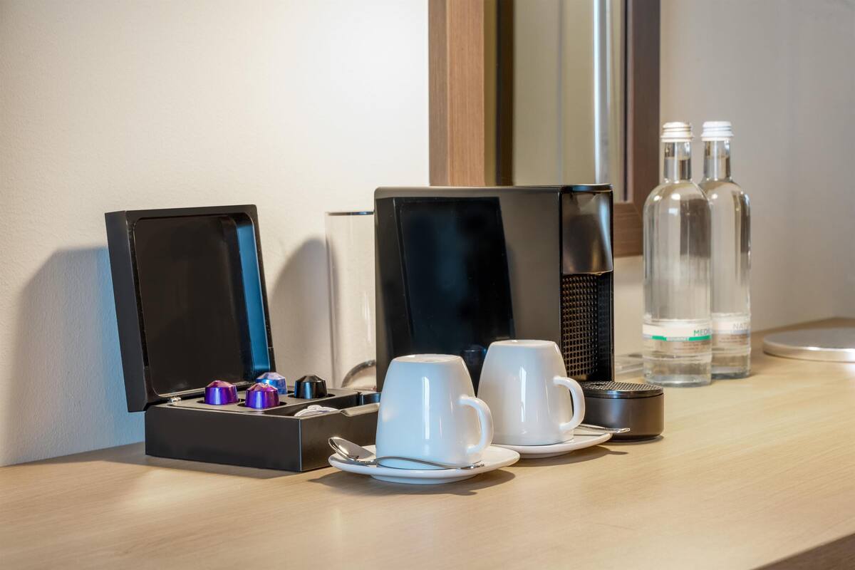 Habitación de hotel con estación de café, dos tazas blancas, una caja y dos botellas.
