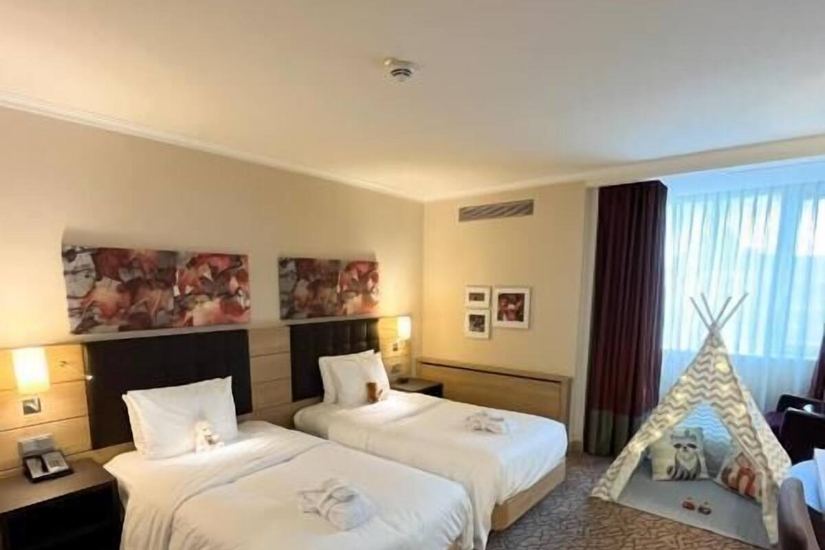 Habitación de hotel con dos camas, una mesita de noche, una ventana con cortinas y una decoración tipo tipi.