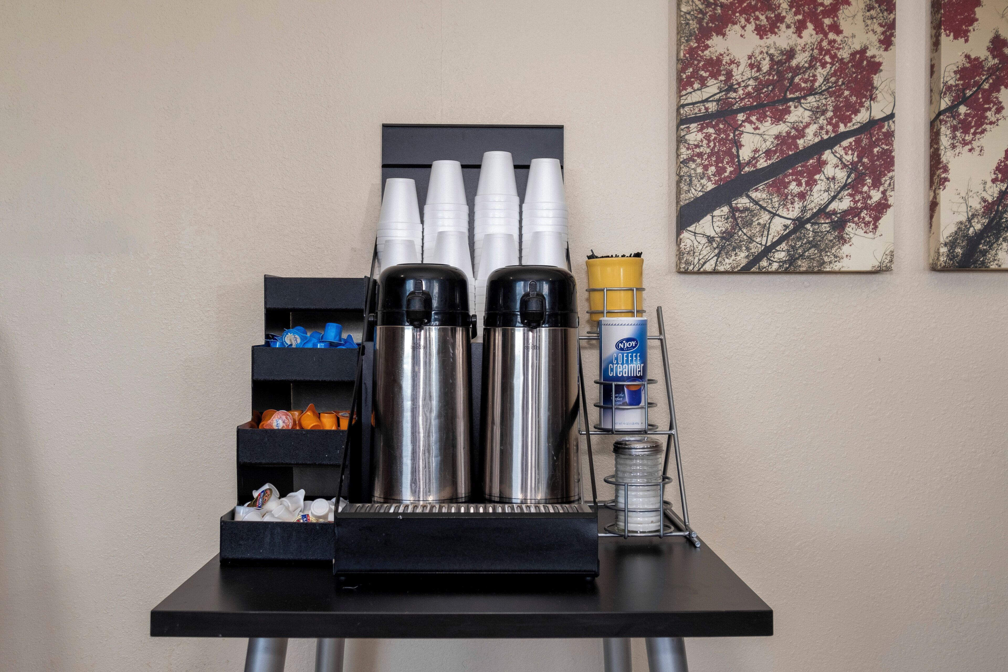 Een koffiehoek met een koffieapparaat, kopjes, room en een roomdispenser.