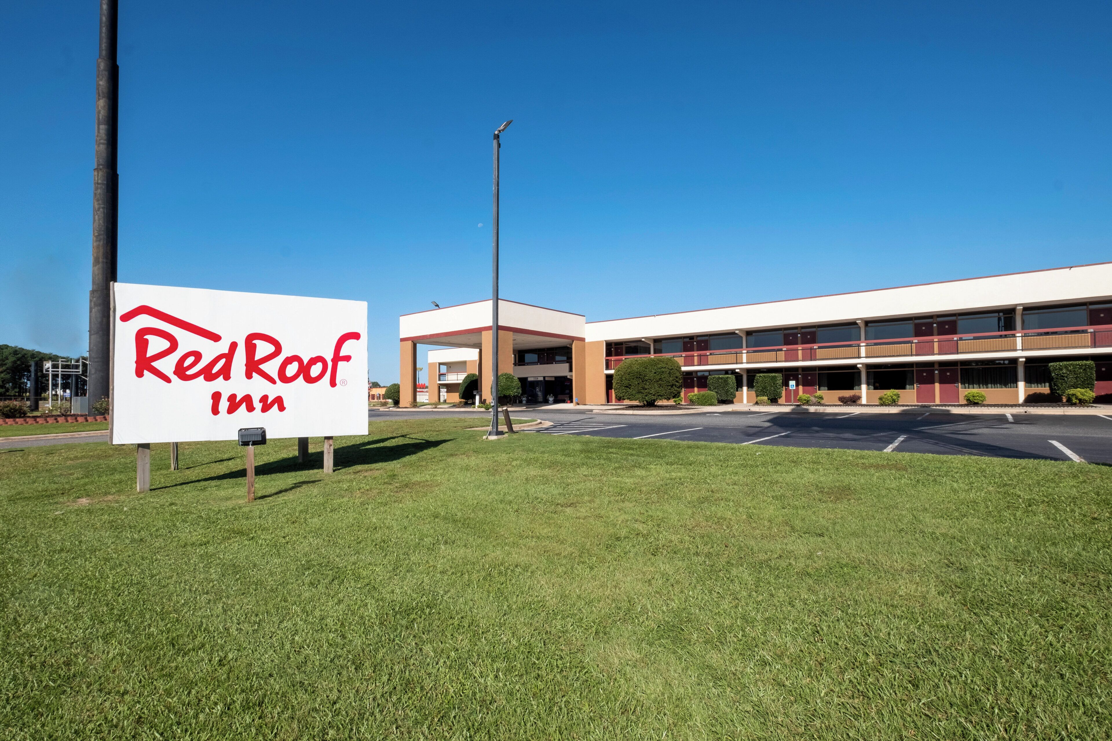 A Red Roof Inn with a clear sky, a parking lot, and a building with multiple floors and a flat roof.