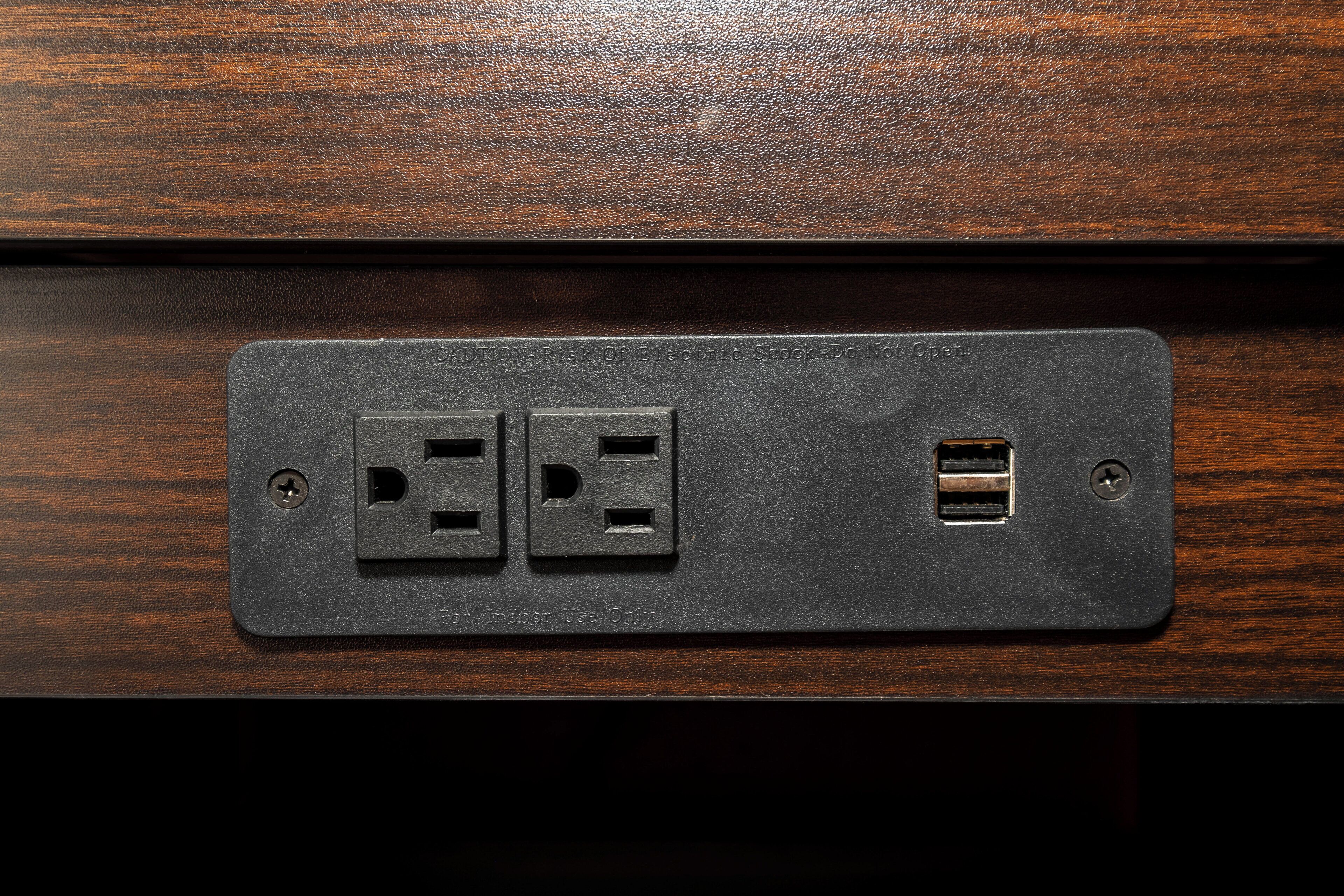 A black electrical outlet with two standard sockets and a USB port on a wooden surface.