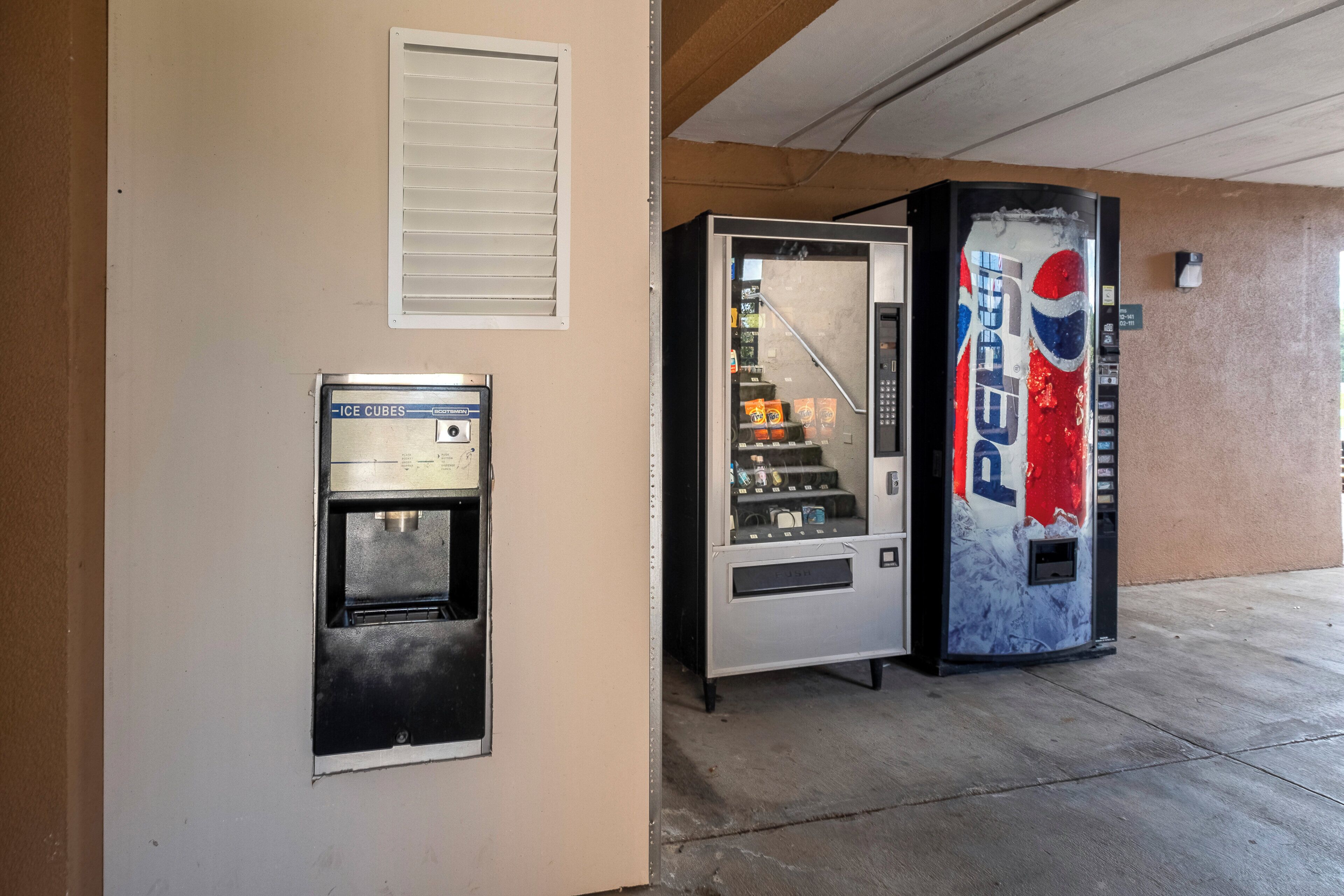A vending machine with a Pepsi logo, a coin-operated ice dispenser, and a small window.