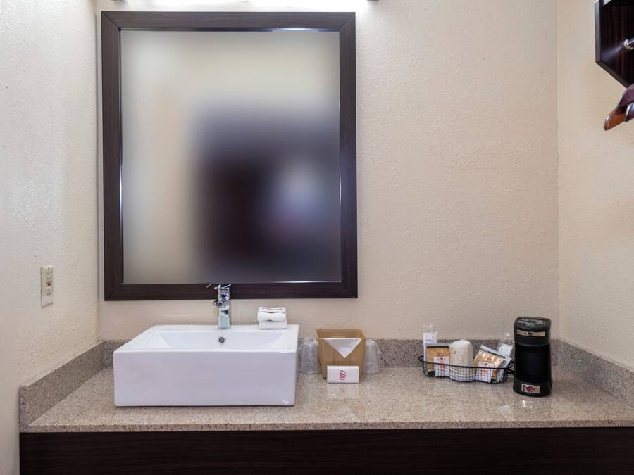 Un bany amb un lavabo blanc, un mirall i una cafetera al taulell.