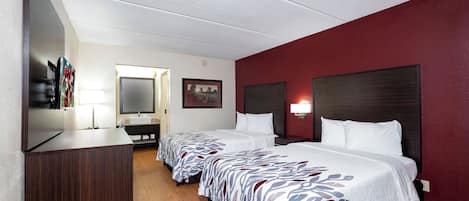 A hotel room with two beds, a TV, a desk, and a mirror.