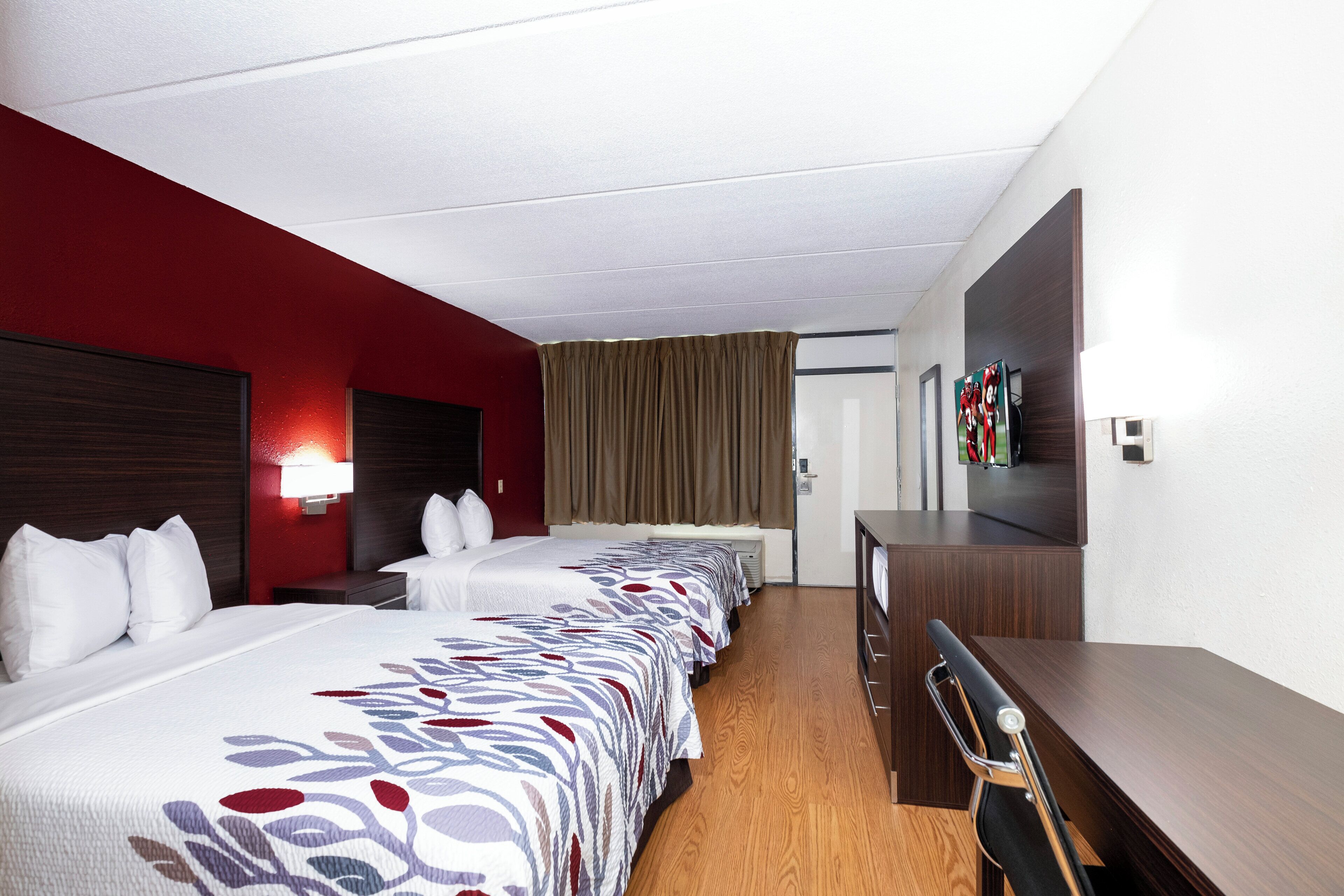 A hotel room with two beds, a desk, a TV, and a door.