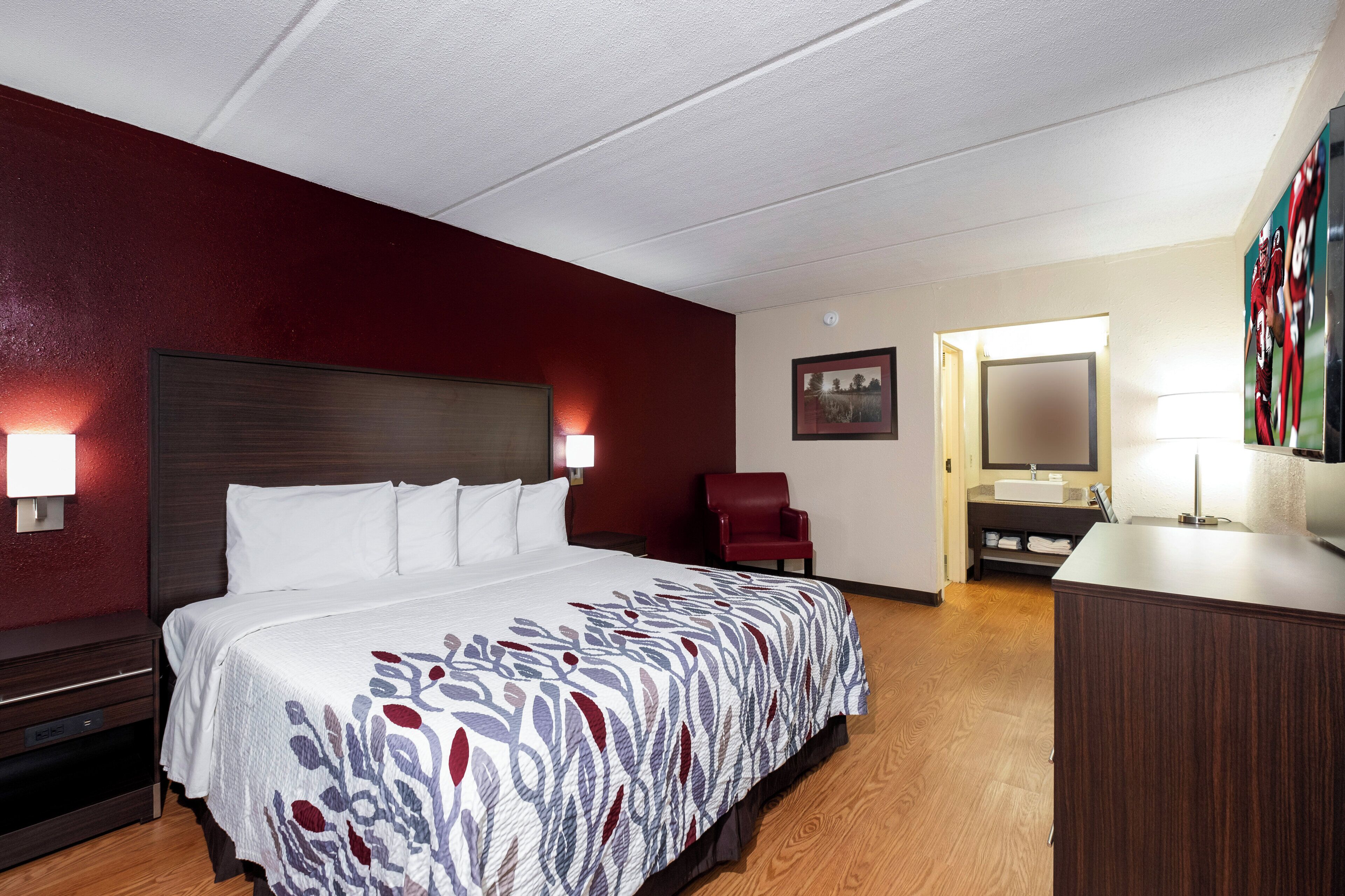 A hotel room with a large bed, a desk, a chair, and a bathroom.