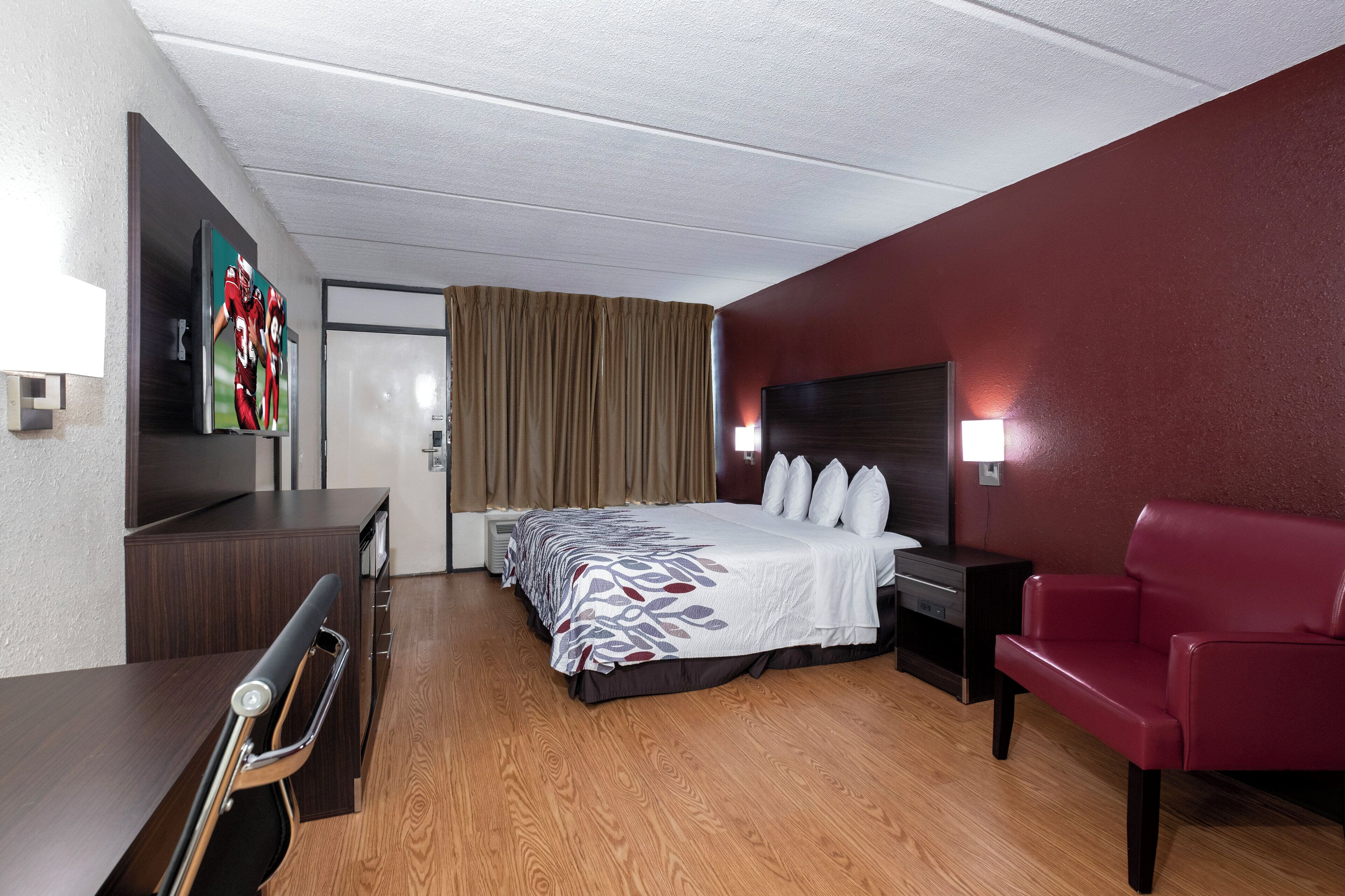 Une chambre d’hôtel équipée d’un lit, d’un bureau, d’une chaise, d’une télévision et d’une lampe fixée au mur.
