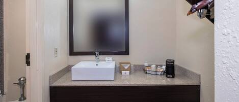 A bathroom with a white sink, dark wooden vanity, a mirror, and a towel rack.