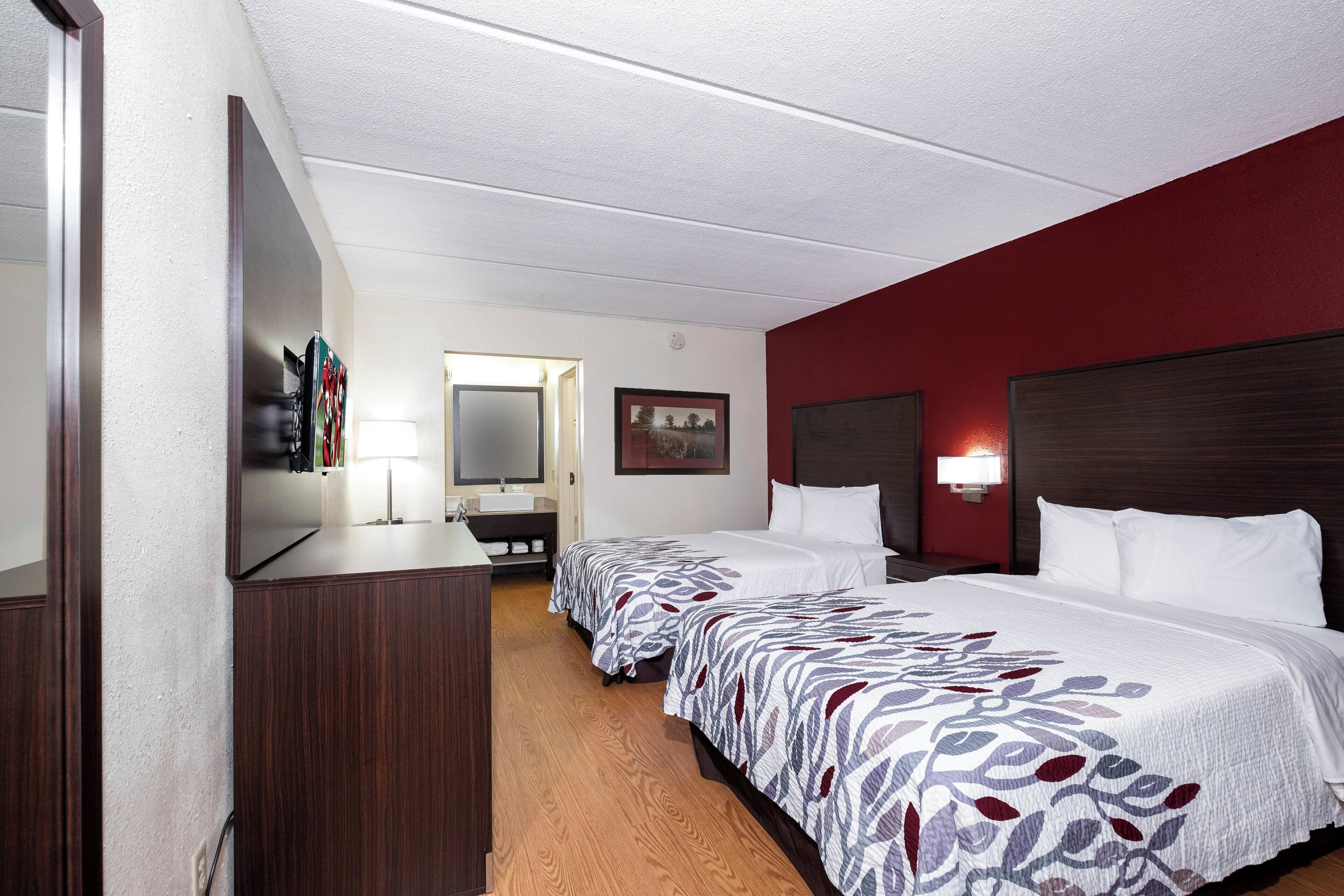 Une chambre d’hôtel avec deux lits, un bureau, un miroir et une télévision.