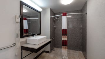 A modern bathroom with a white sink, a large mirror, and a shower with a red and white curtain.