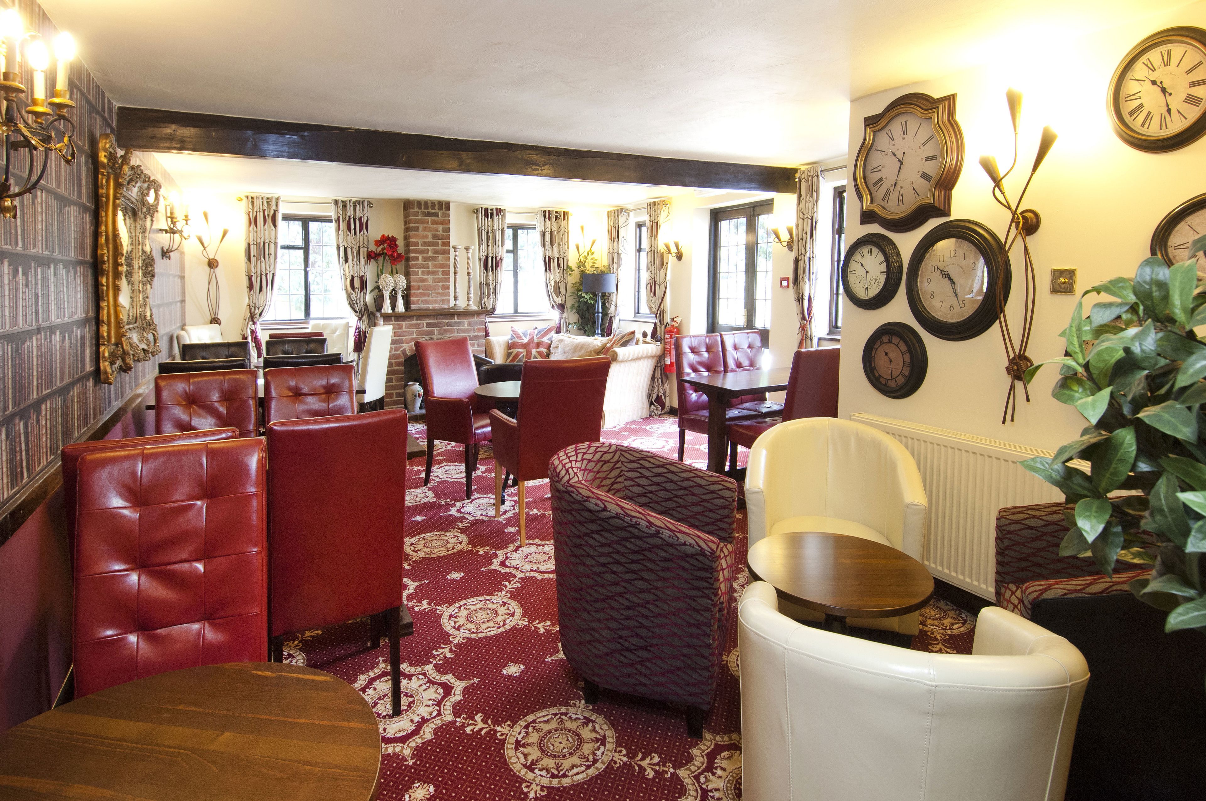A dining area with red upholstered chairs, a patterned rug, and a variety of clocks on the wall.