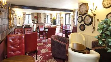 A dining area with red upholstered chairs, a patterned rug, and a variety of clocks on the wall.