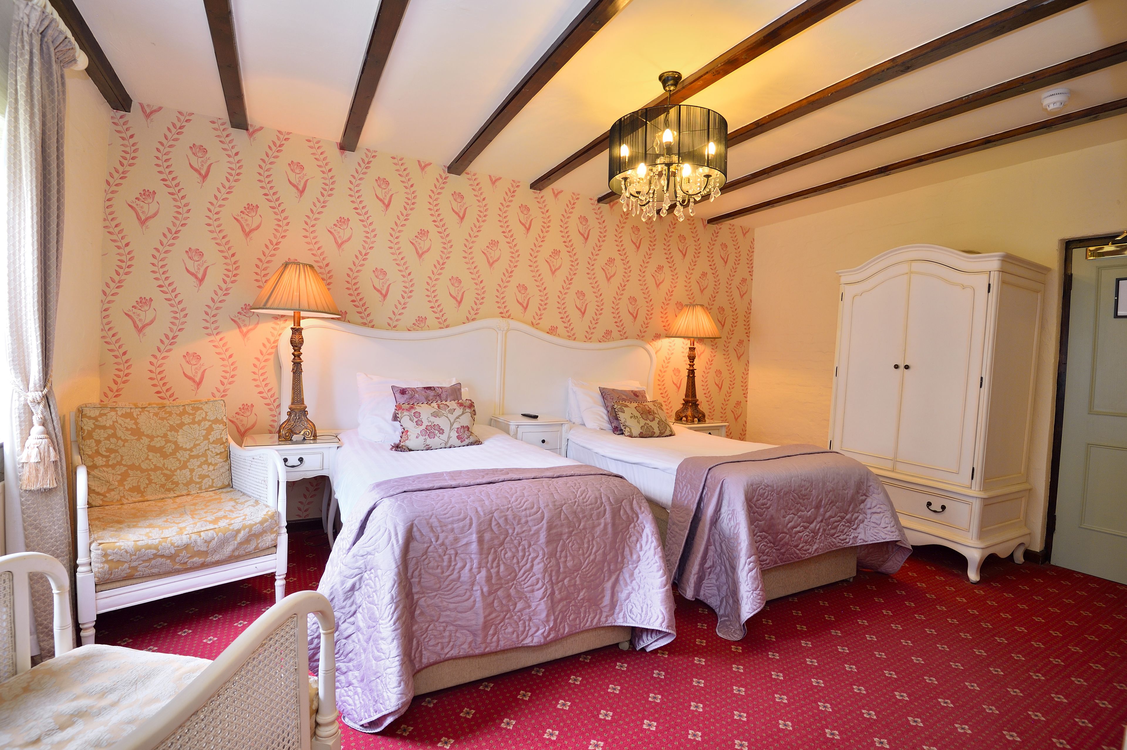 A bedroom with two beds, a chair, a wardrobe, and a chandelier.