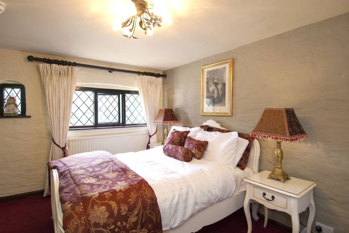 A neatly arranged bedroom with a bed, two bedside tables, a window with curtains, a wall-mounted picture, and a ceiling light fixture.