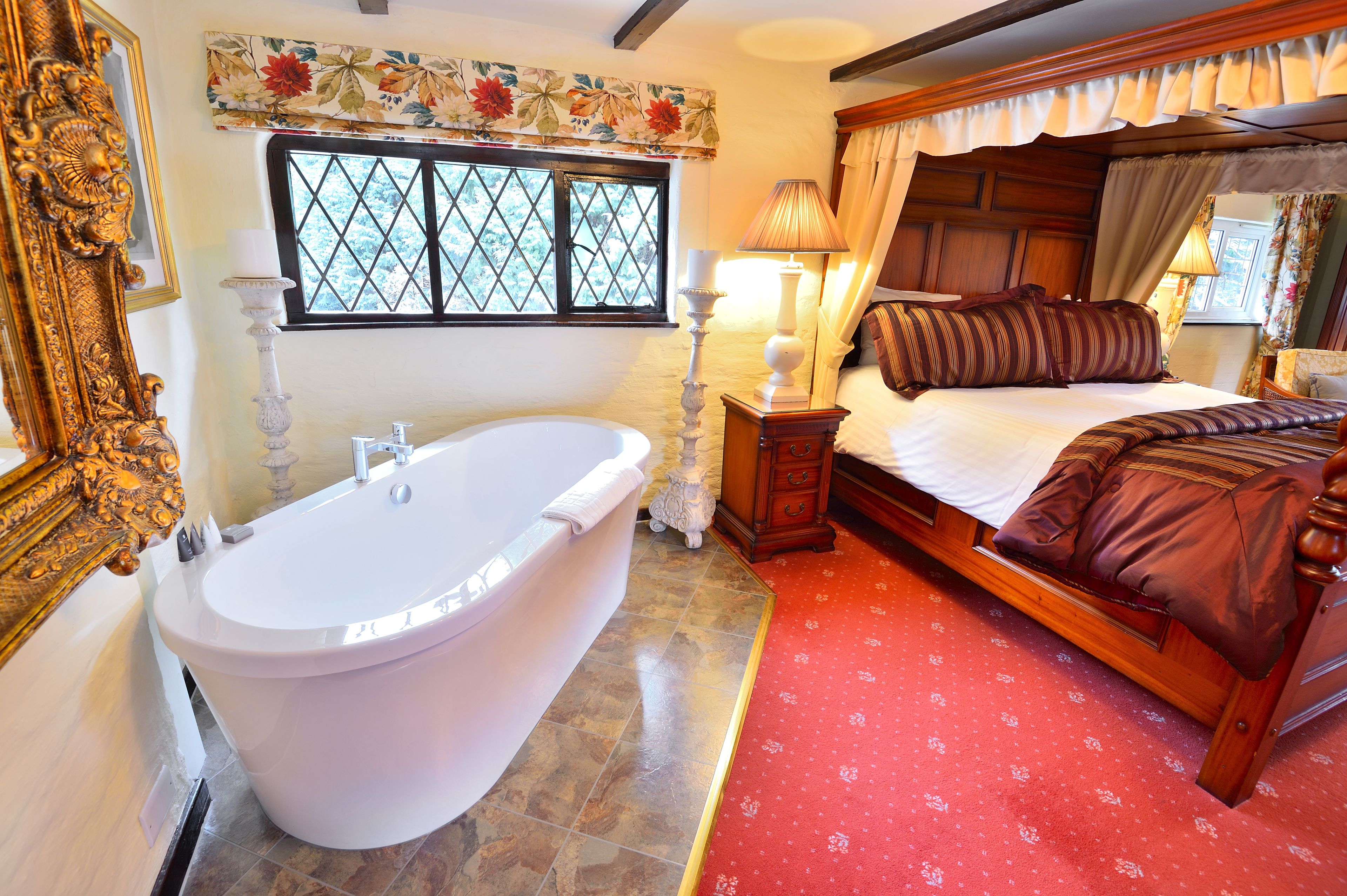 A bedroom with a large bathtub, a wooden bed with a canopy, and a window with floral curtains.