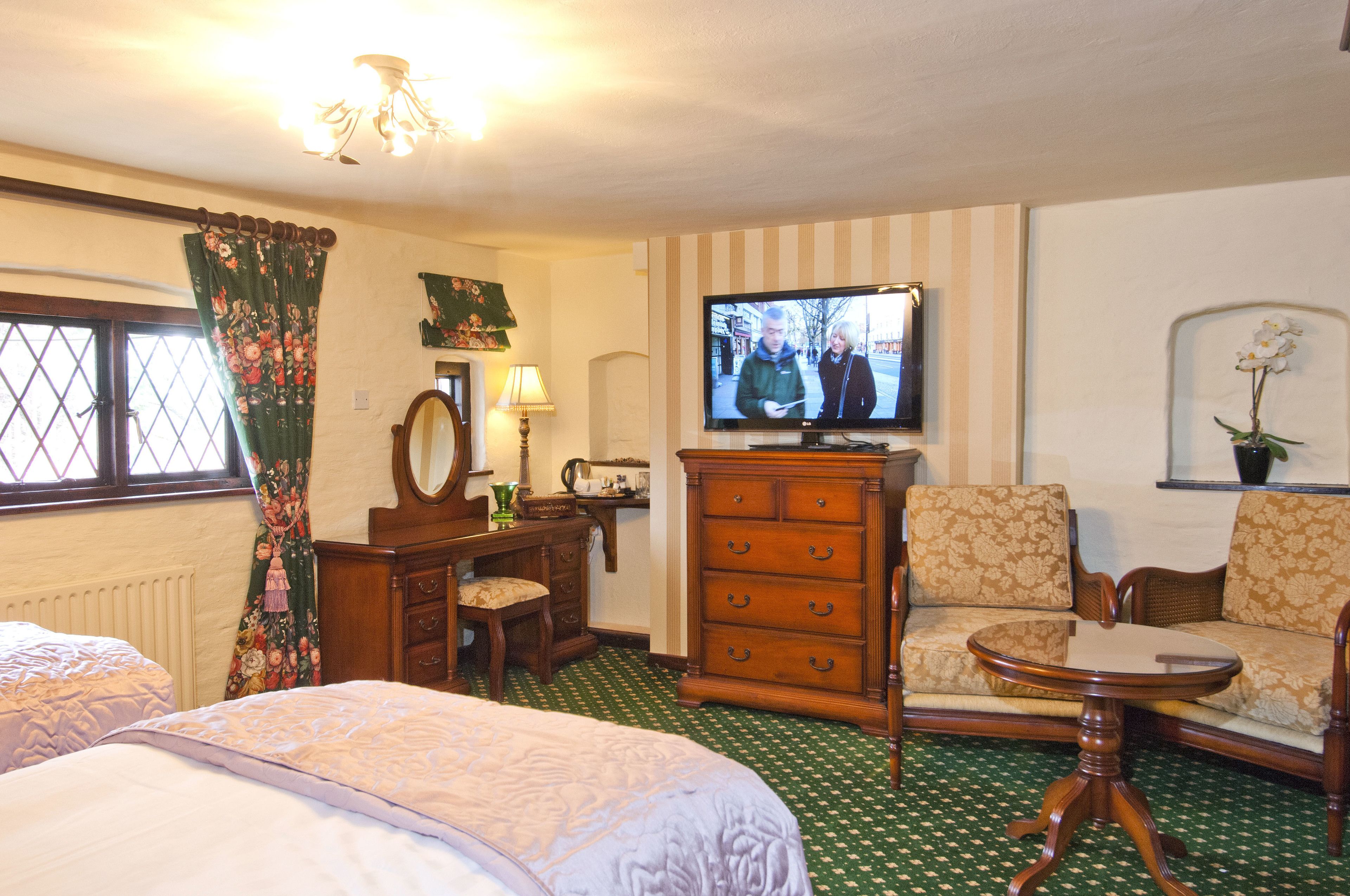 Una habitación con cama, sofá, televisor, cómoda y ventana con cortinas.