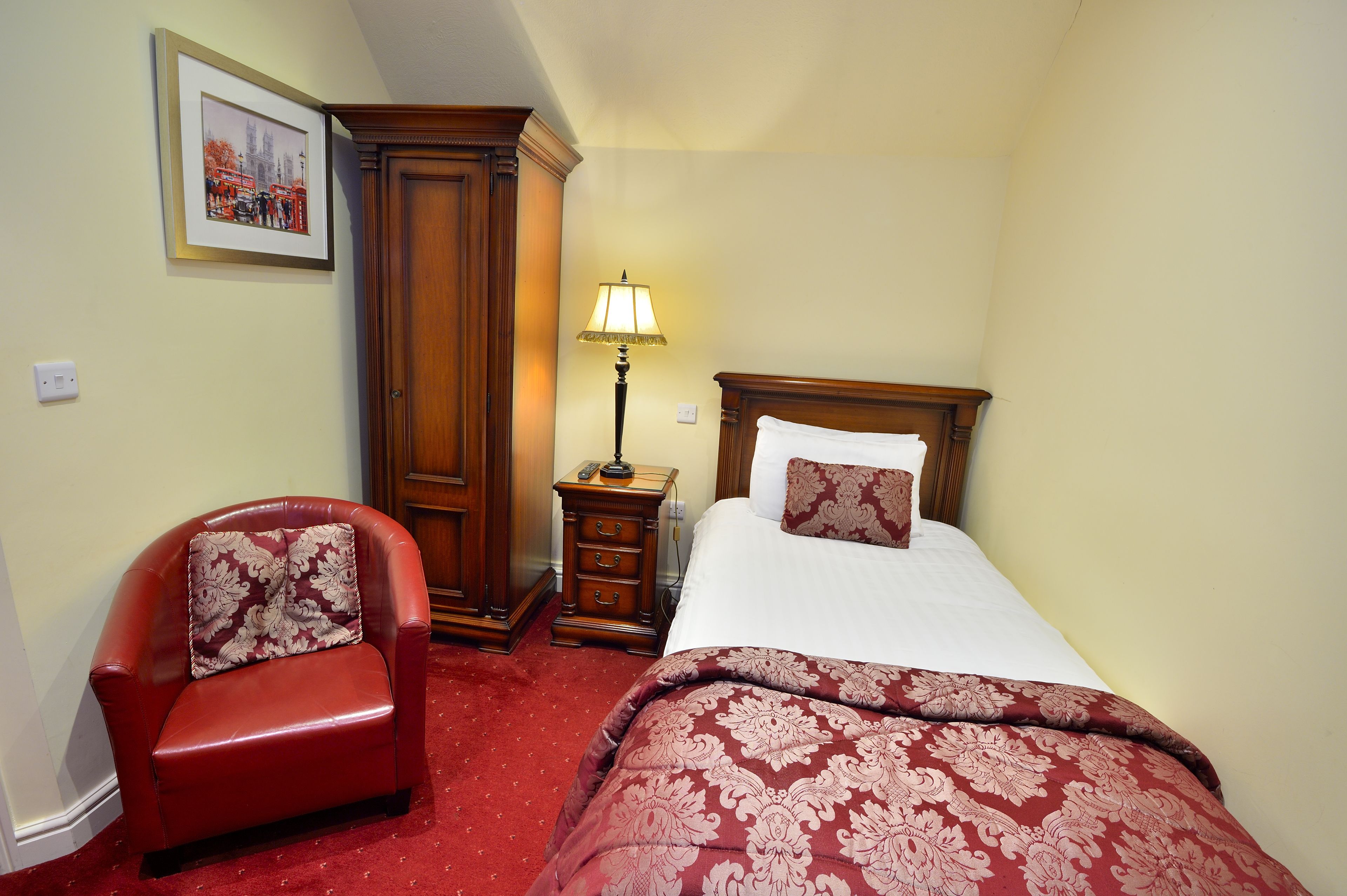 A hotel room with a bed, a chair, a nightstand, and a lamp.