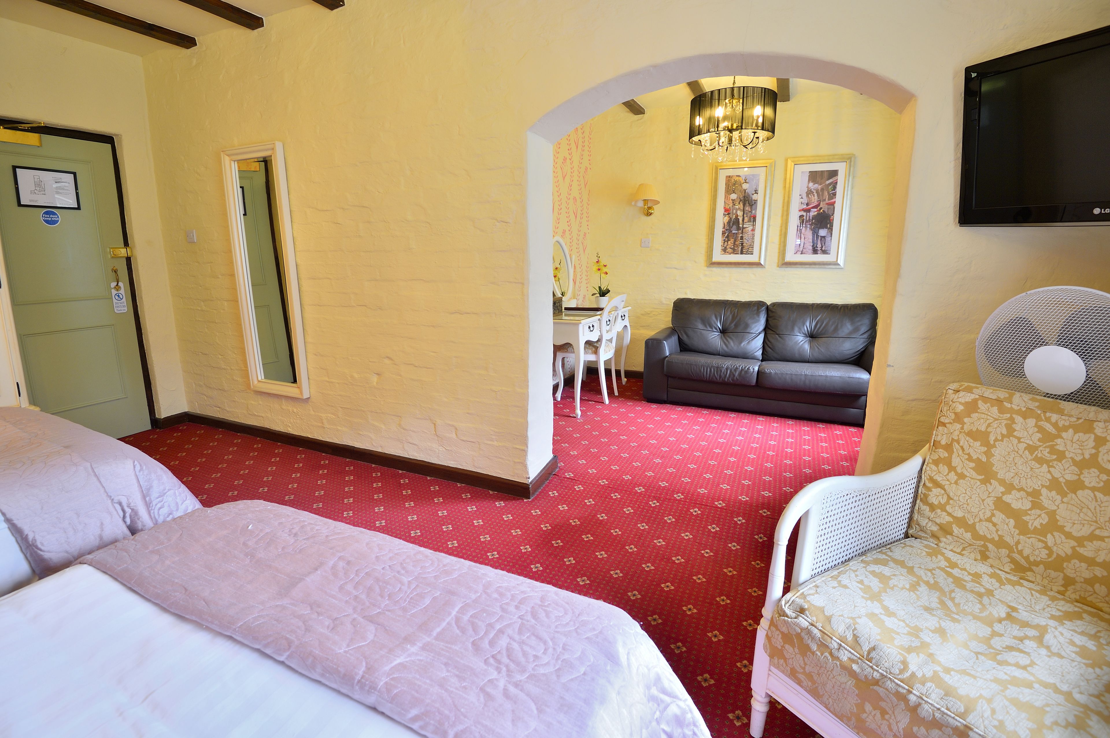 A hotel room with two beds, a sofa, a TV, and a mirror.