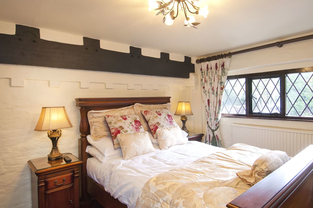 A bedroom with a wooden bed, floral bedding, two bedside lamps, and a window with a view.