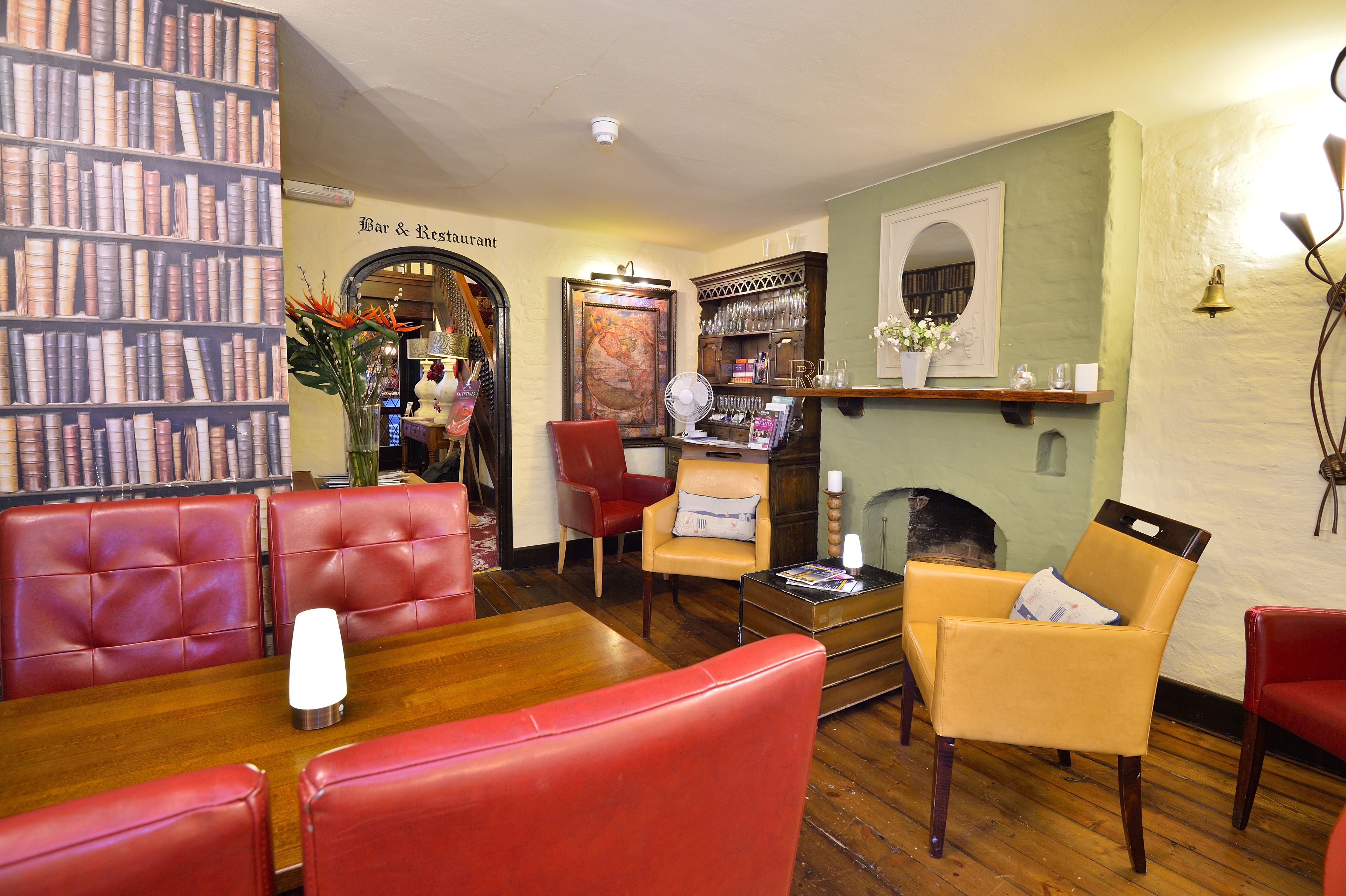 A cozy bar and restaurant interior with leather seating, a fireplace, and a bookshelf.