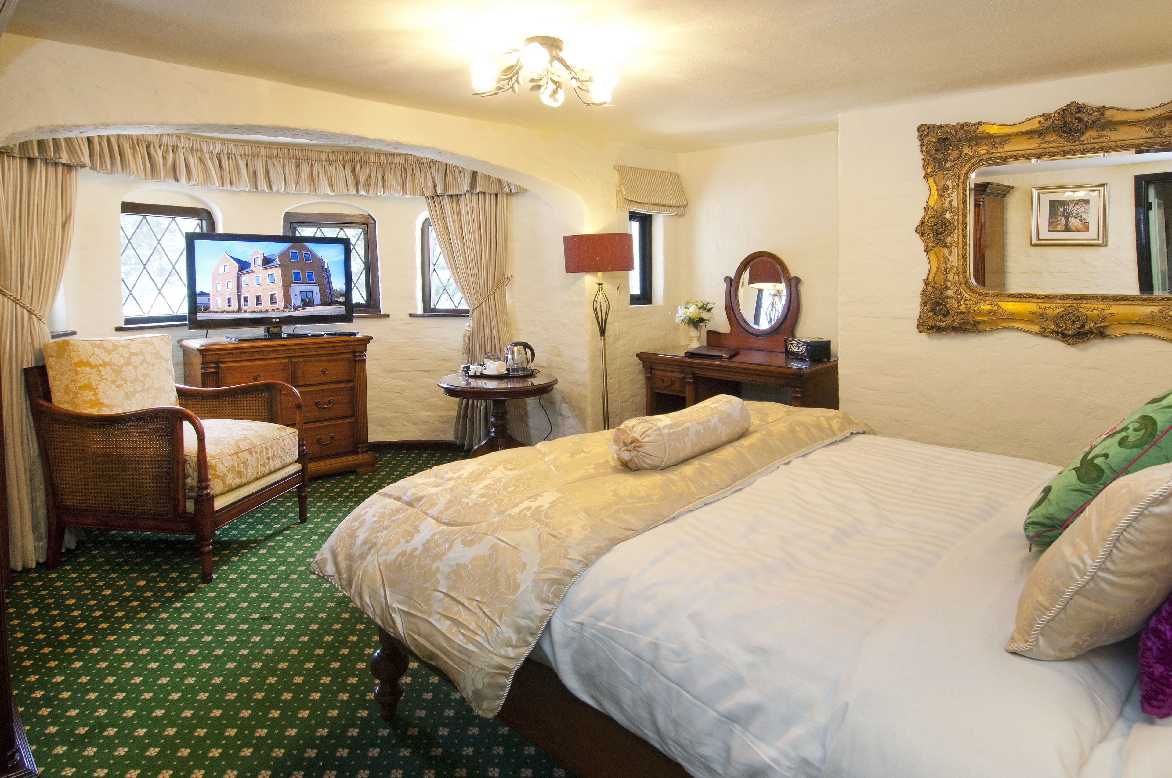 A hotel room with a bed, a chair, a dresser, a television, and a window with curtains.