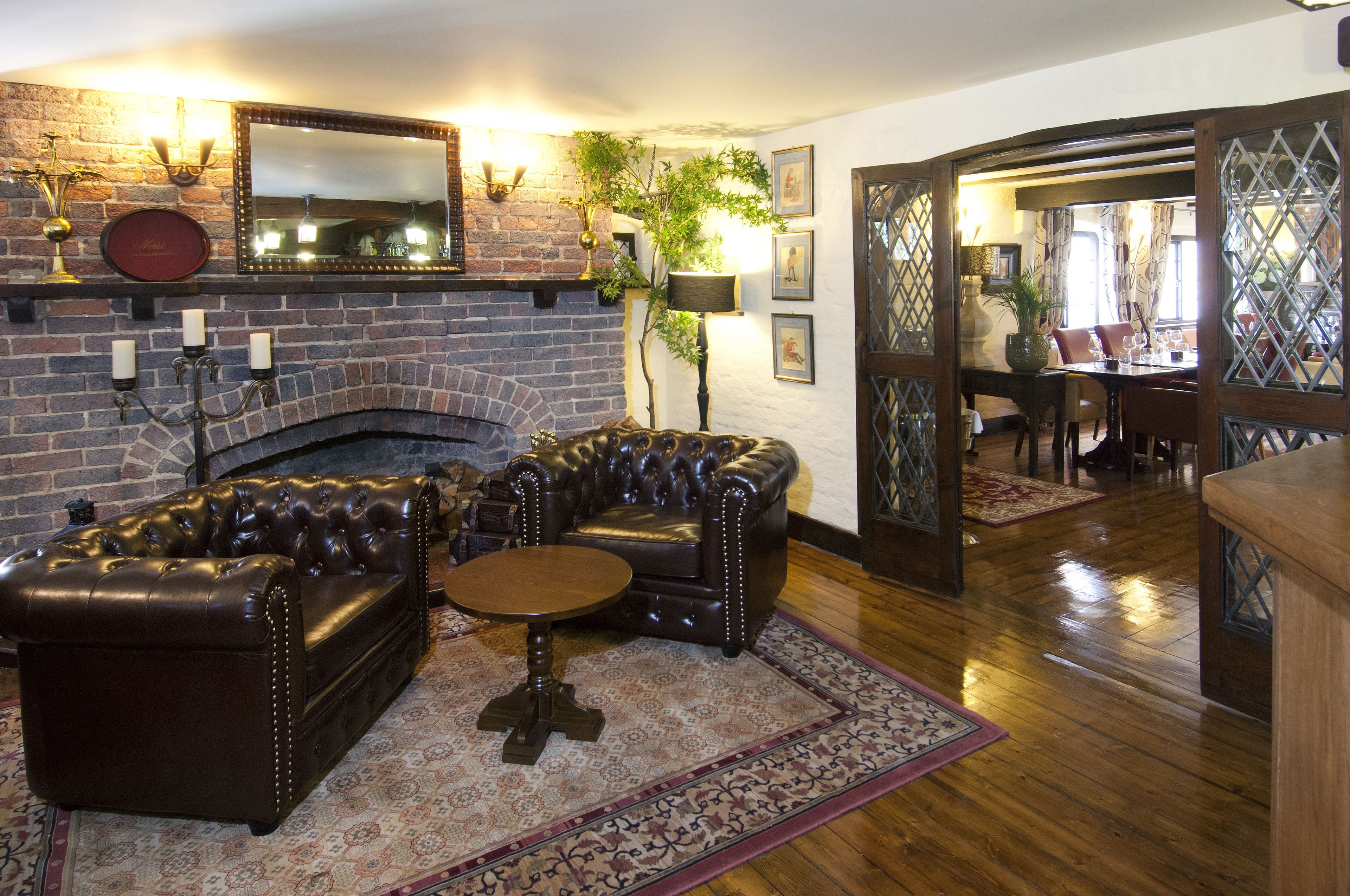 Ein gemütliches Wohnzimmer mit Kamin aus Backstein, Ledersofas und einem Essbereich im Hintergrund.