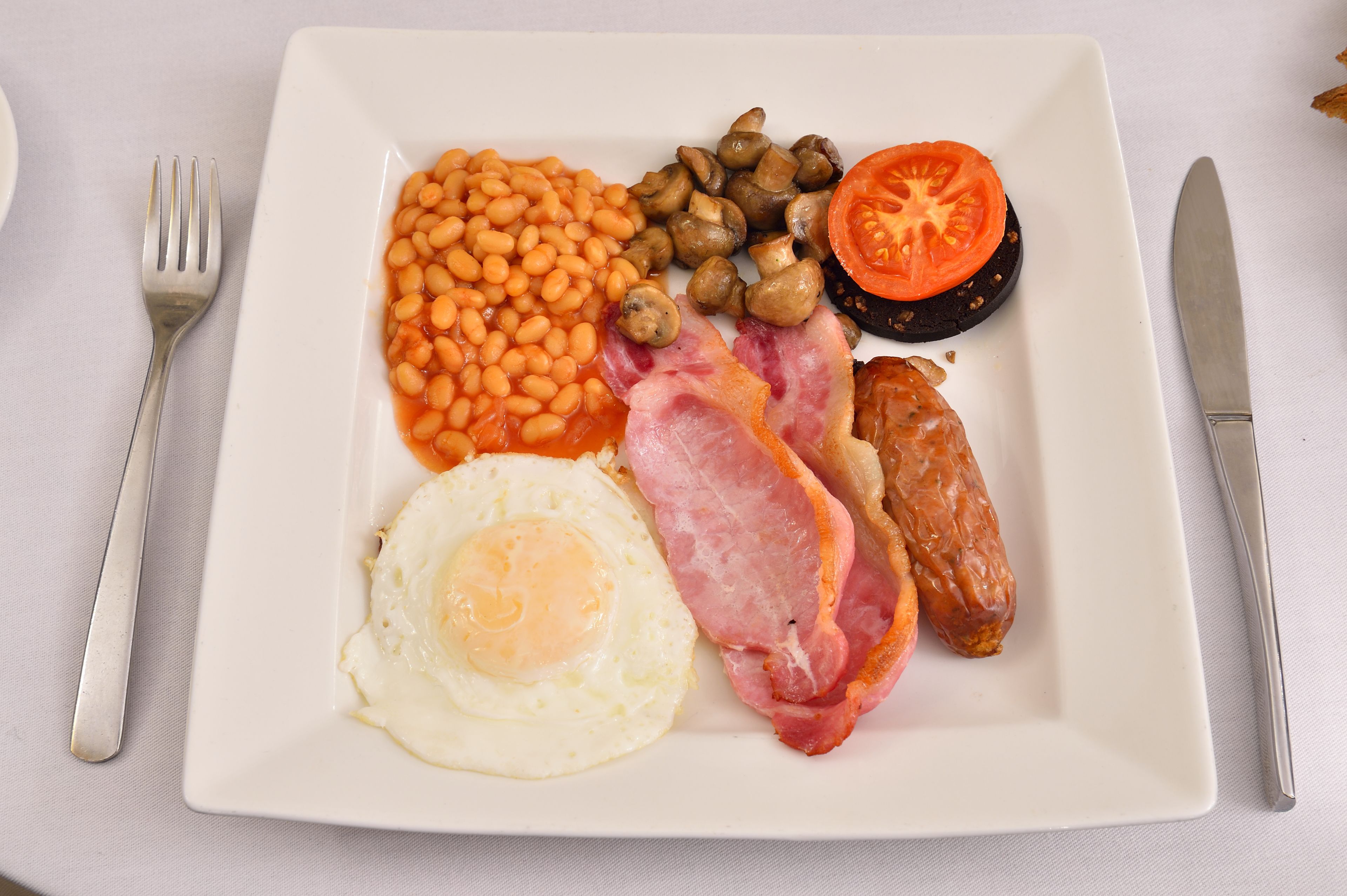 Ein Teller mit Frühstücksei, Speck, Bohnen, Pilzen und einer Tomatenscheibe.