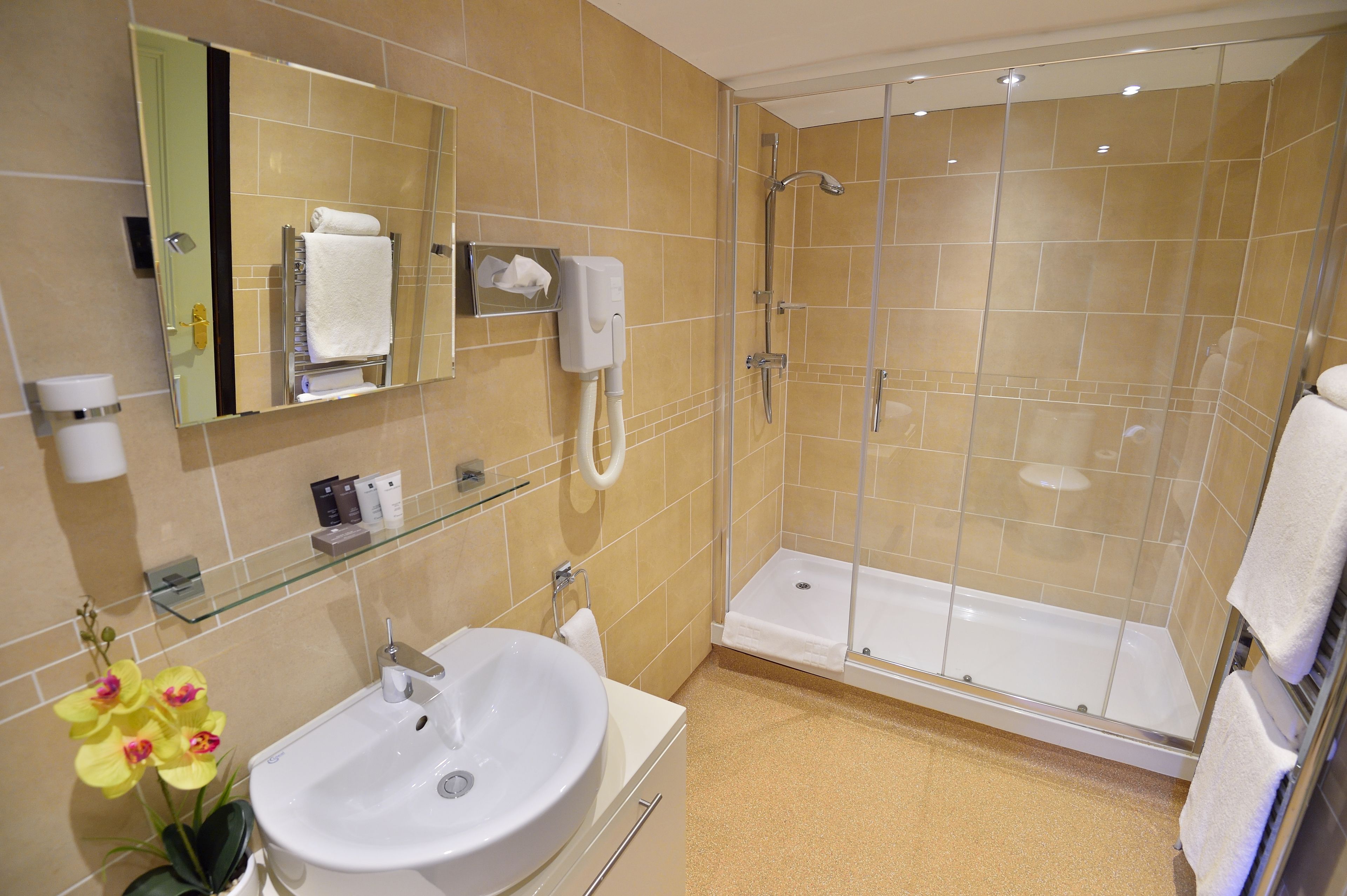 Un baño moderno con ducha de vidrio, un lavamanos blanco y un espejo con dispensador de pañuelos.