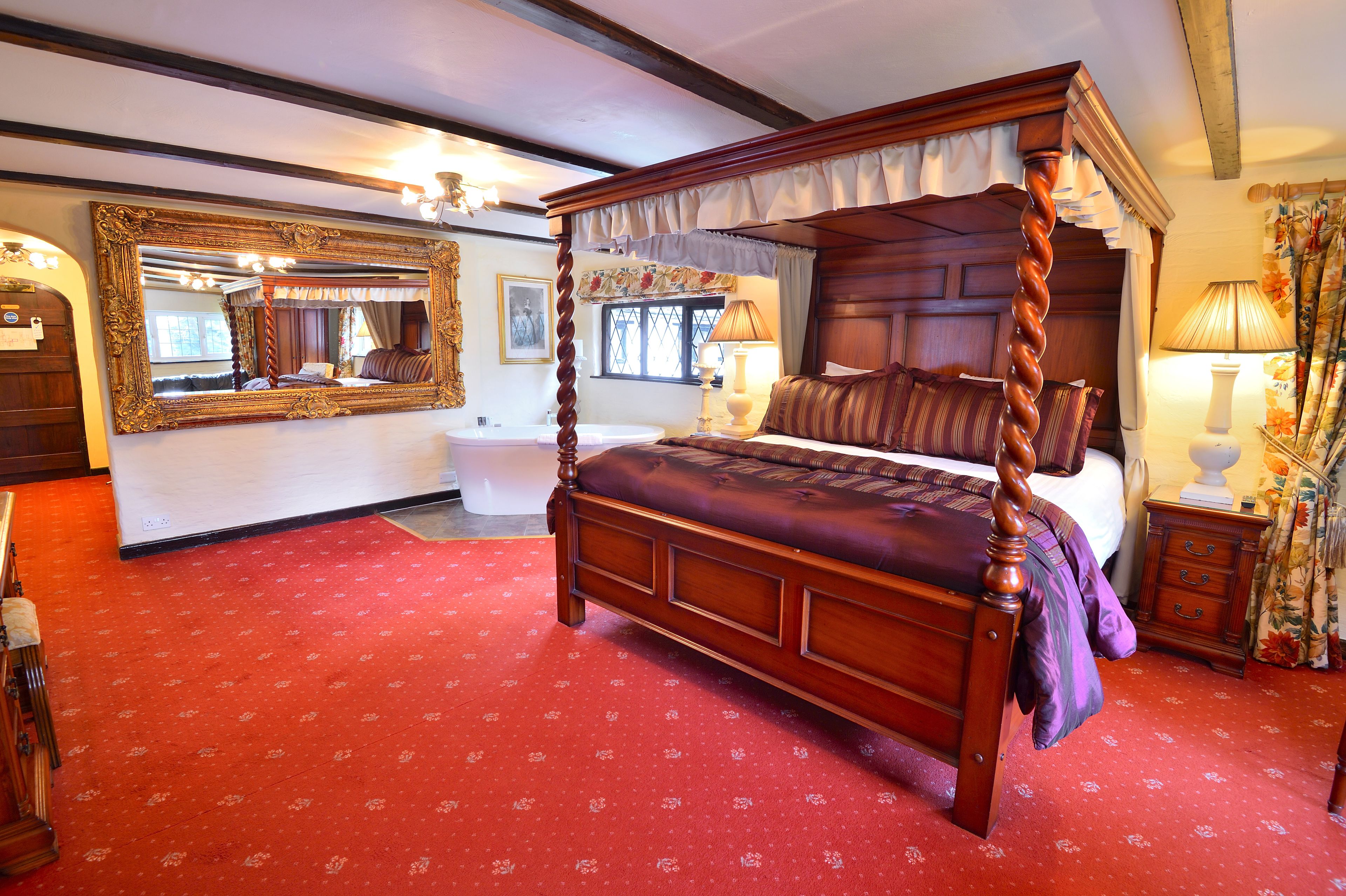 Un lit à baldaquin, un grand miroir décoratif et un tapis rouge à motifs.
