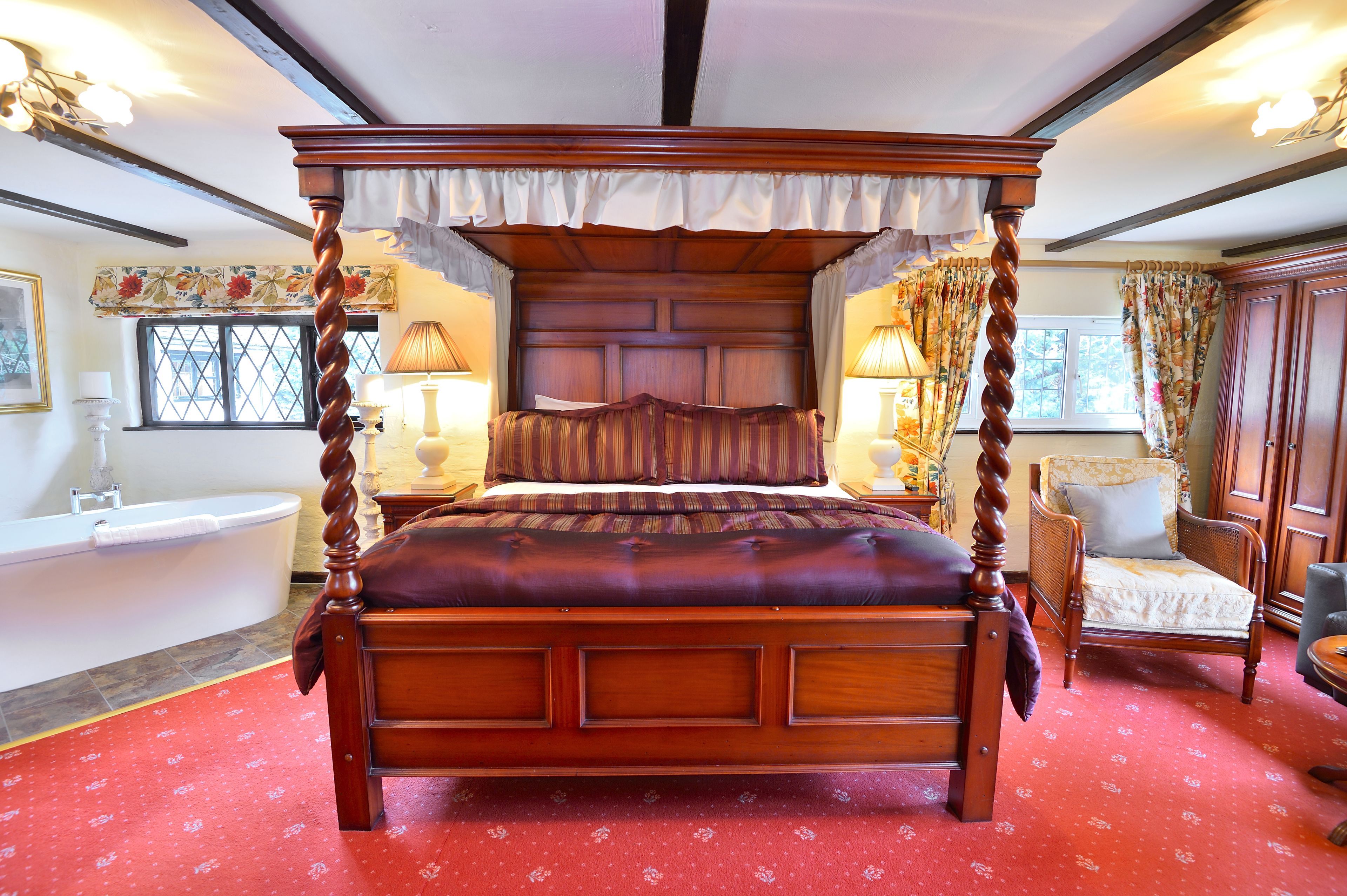 A four-poster bed with a canopy, a sitting chair, a small table, and a bathtub.