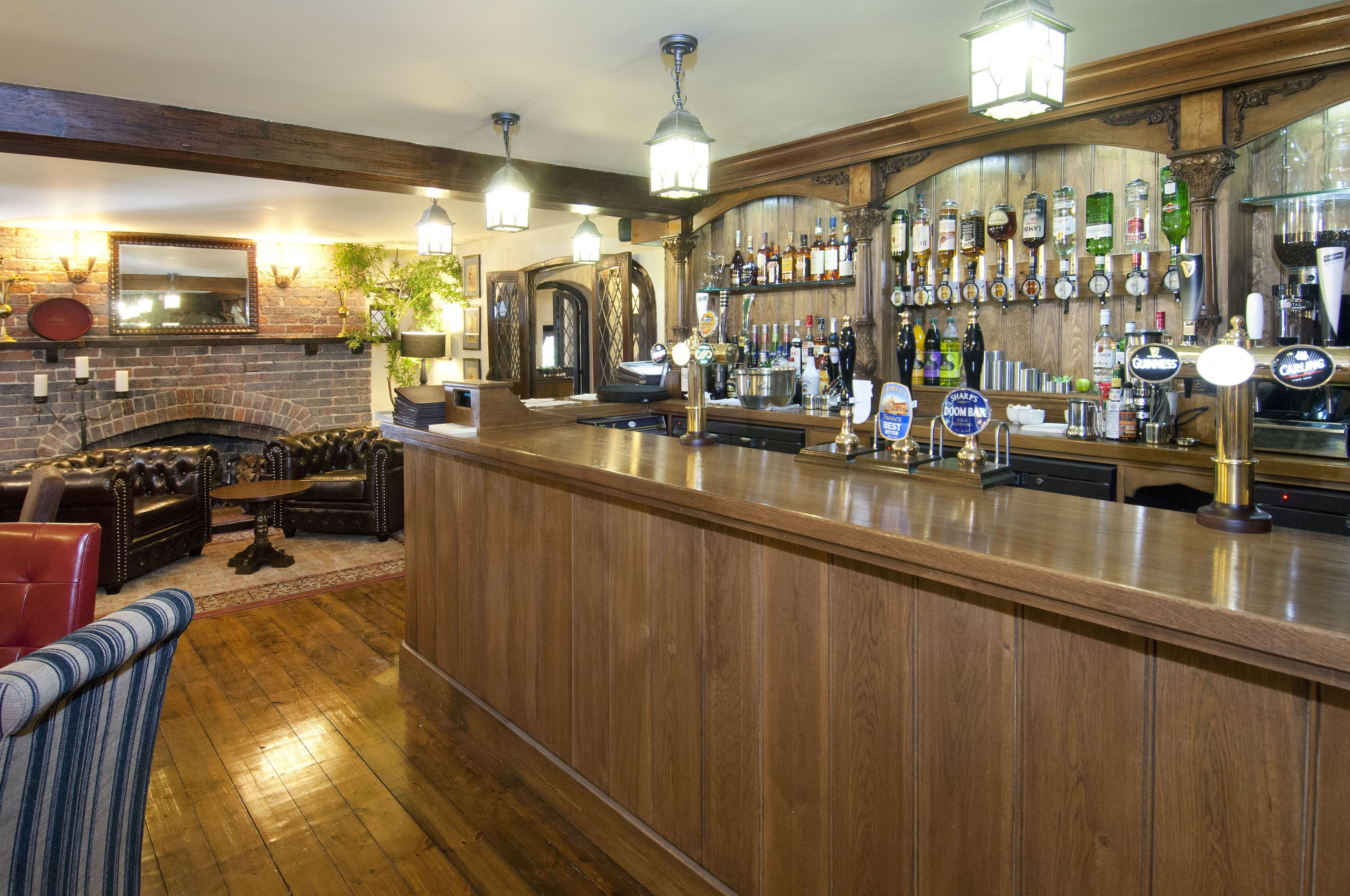 Un espace bar avec un comptoir en bois, des étagères remplies de bouteilles et une cheminée.