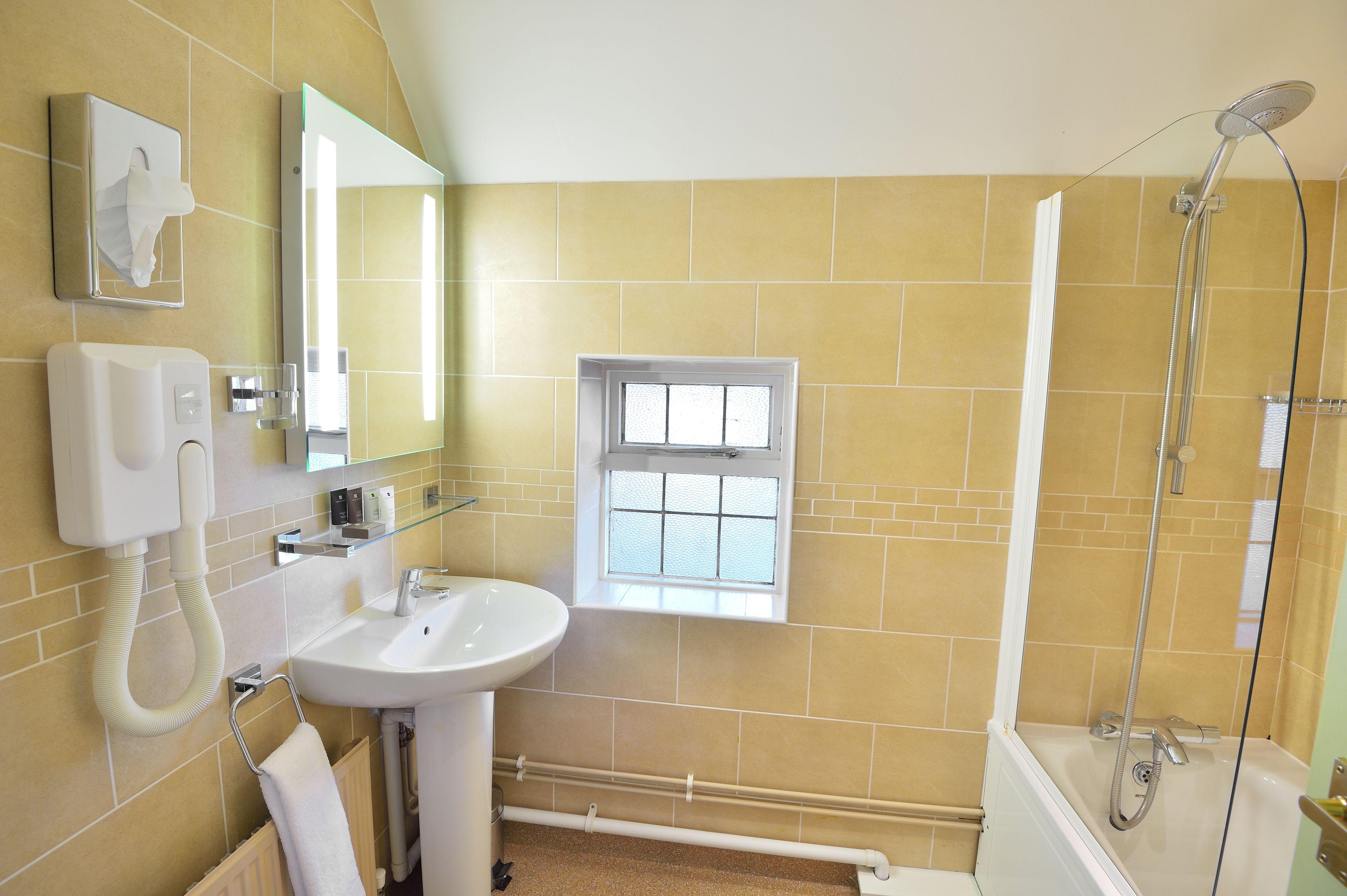 A bathroom with a sink, mirror, towel rack, window, and shower.
