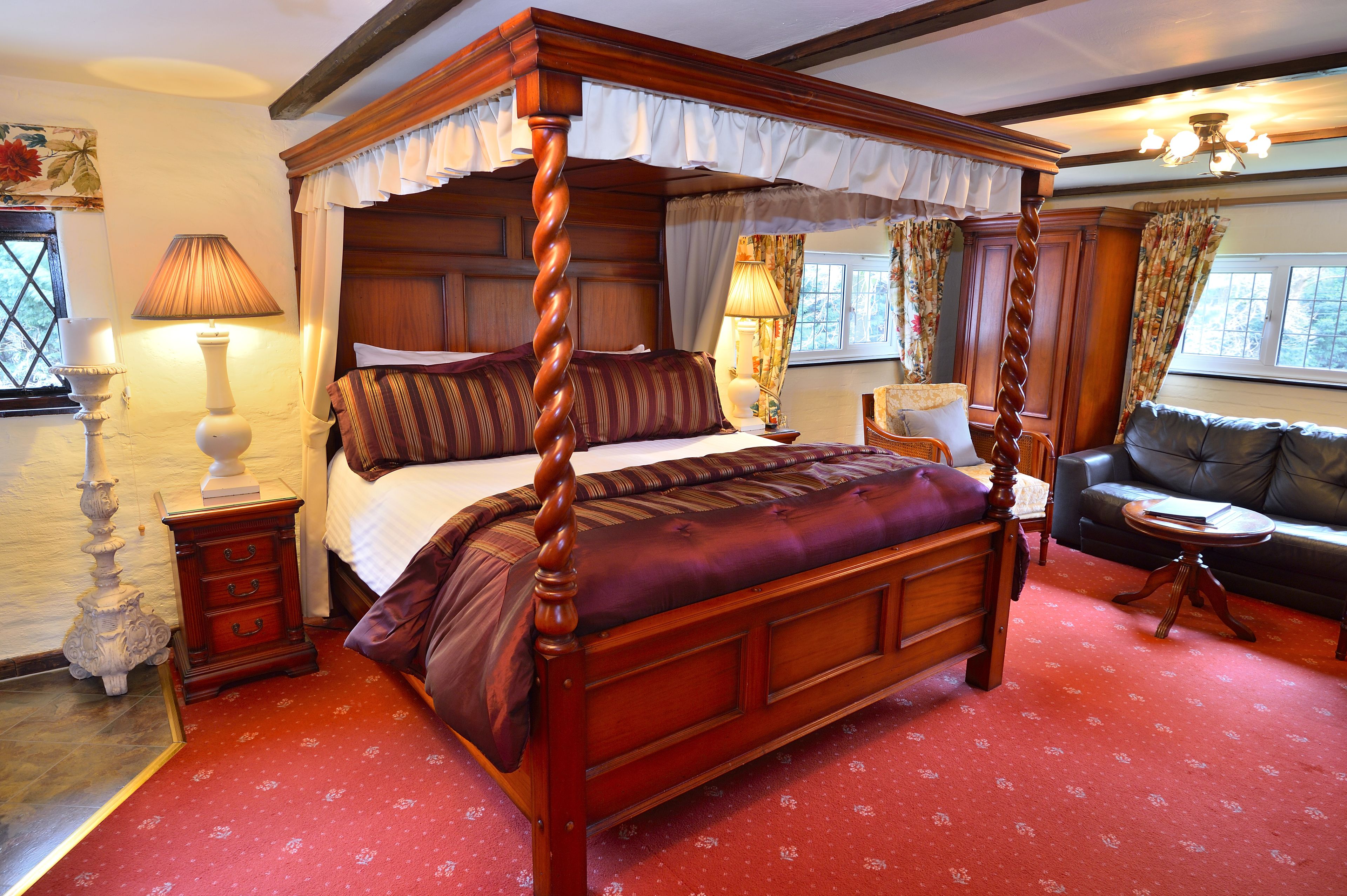 A four-poster bed with a canopy, a sofa, and a small round table in a room with patterned carpet.