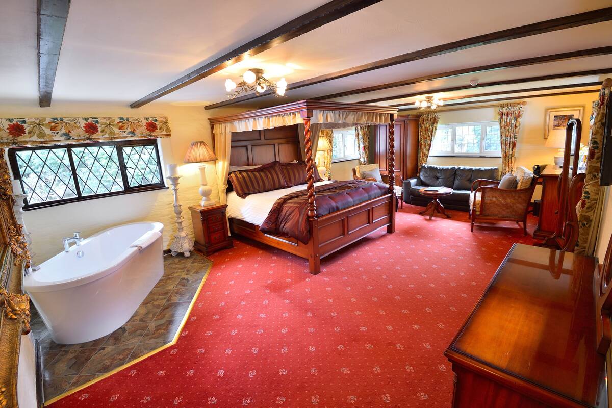 A four-poster bed with a canopy, a clawfoot bathtub, and a wooden bench.