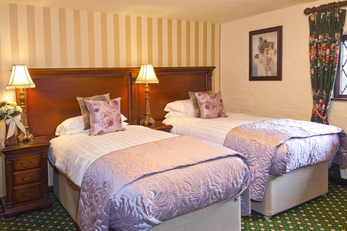 A hotel room with two beds, a wooden headboard, bedside lamps, floral-patterned pillows, and a framed picture on the wall.