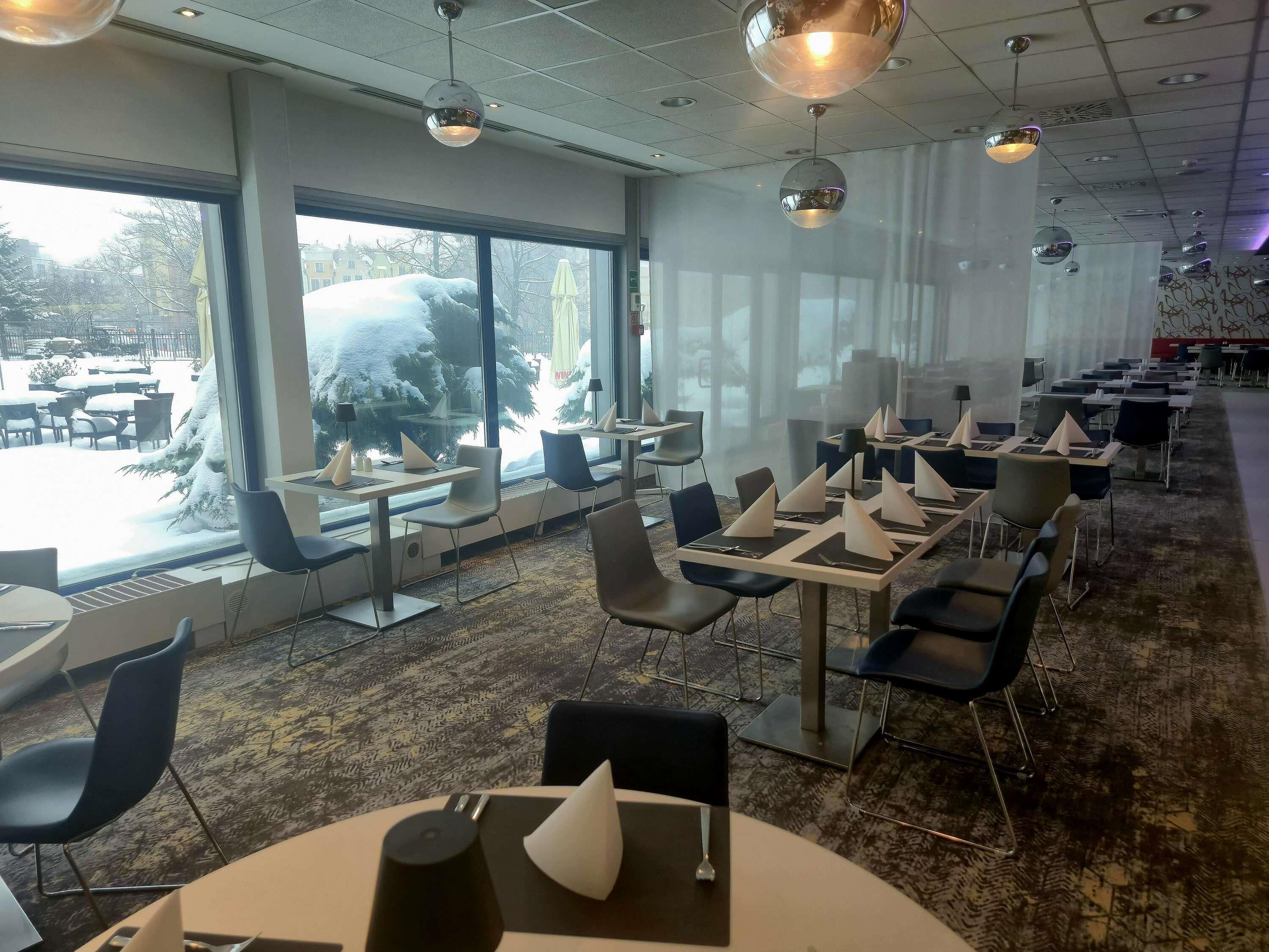 A modern restaurant with large windows, tables with napkins, and a carpeted floor.