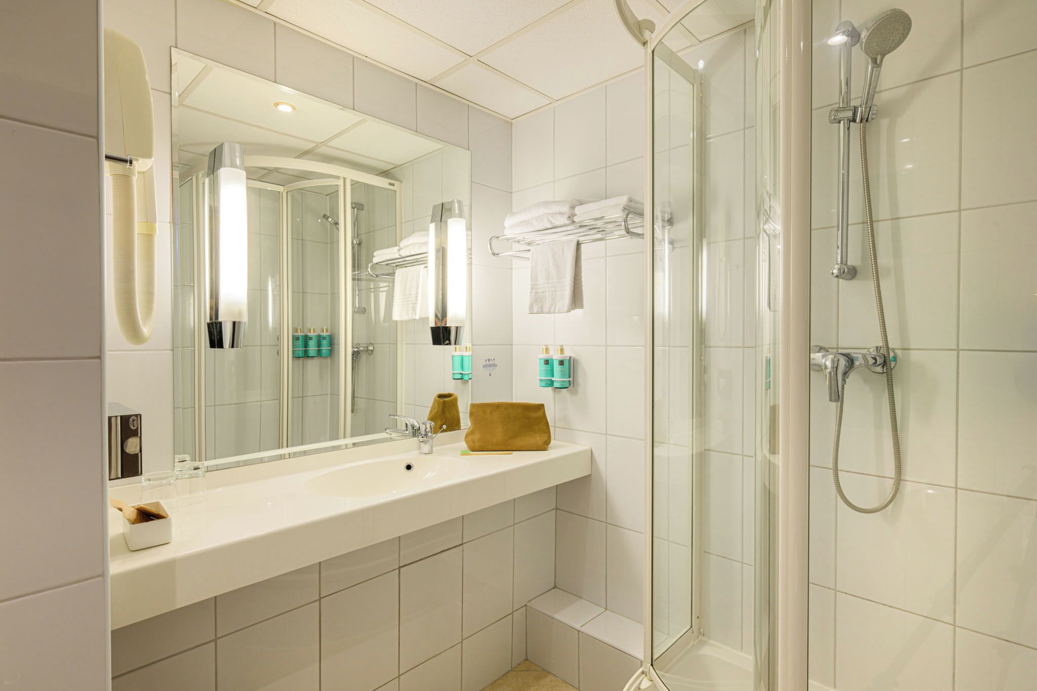 A modern bathroom with a glass-enclosed shower, a large mirror, and a white sink with toiletries.