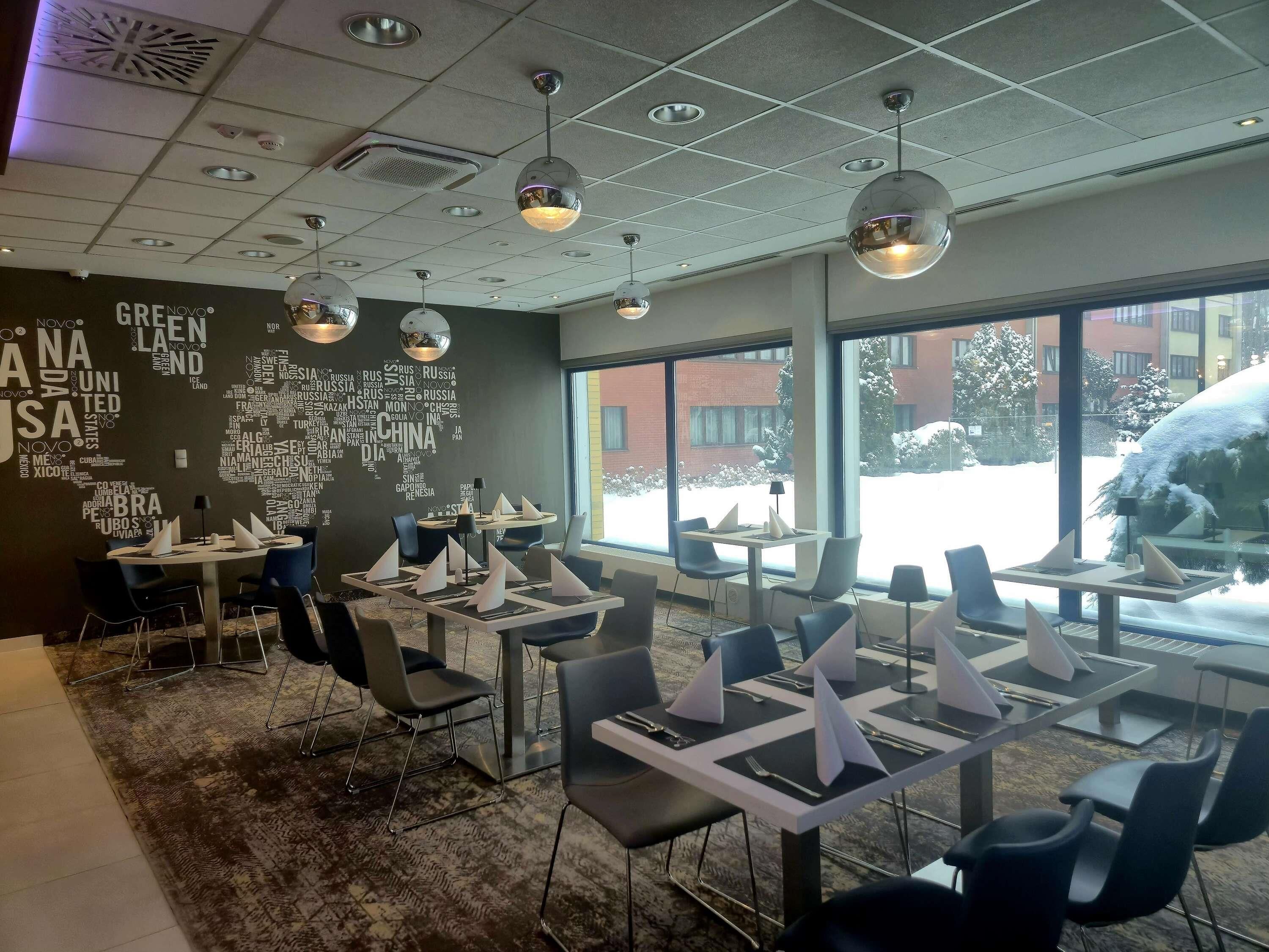 Un espace de restauration moderne avec des tables dressées, un mur décoré d’un nuage de mots et de grandes fenêtres offrant une vue sur un paysage enneigé.