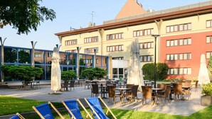 Een hotelterras met buitenmeubilair, een gazon en een gebouw met veel ramen en een rood dak.