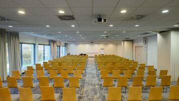 Un salón de conferencias con filas de sillas amarillas, un proyector y suelo alfombrado.