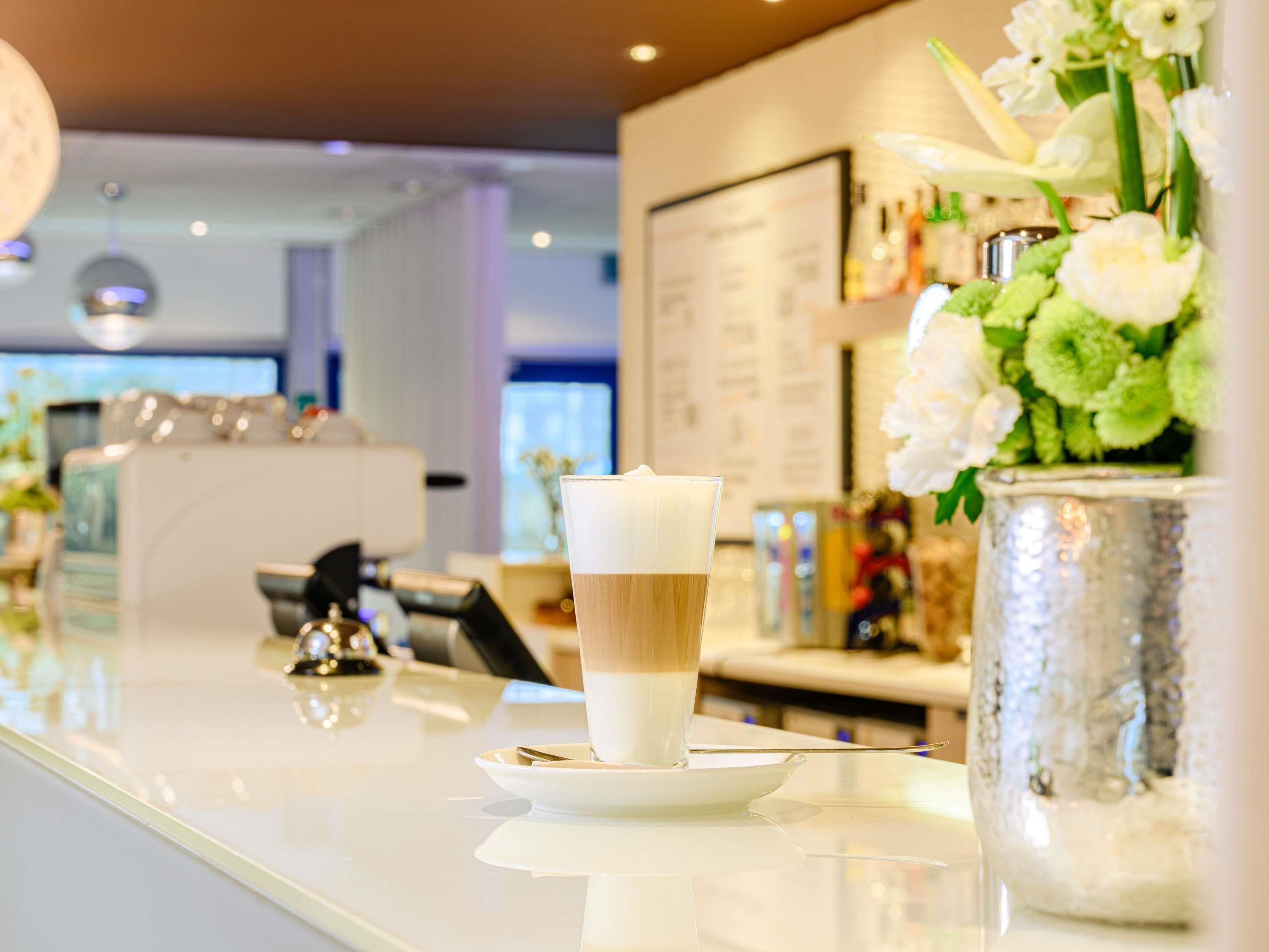 A bar area with a glass of layered drink on a white plate, a cash register, and a decorative vase with flowers.