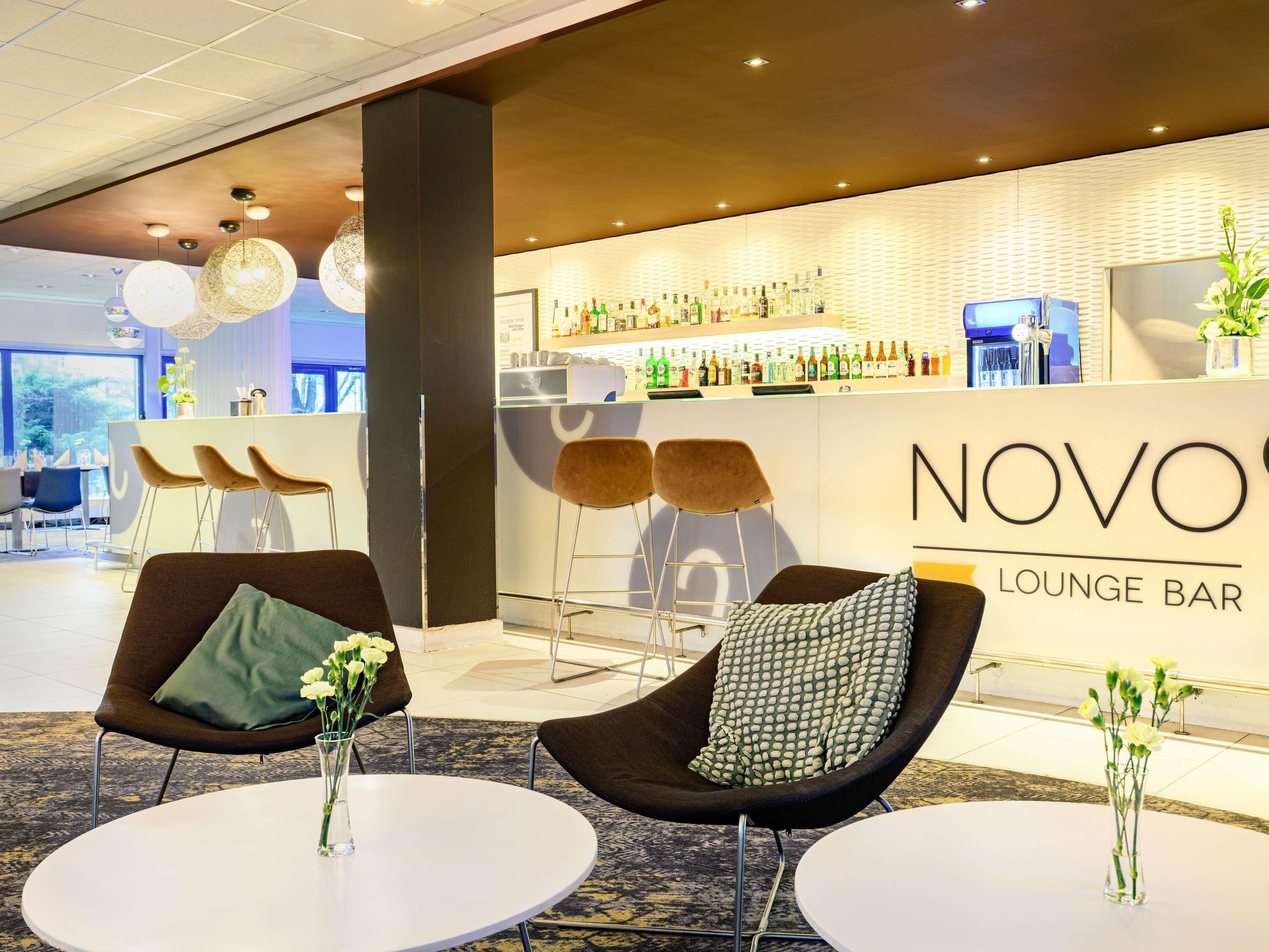 A lounge bar with a bar area, two chairs with cushions, and a vase with flowers on a table.